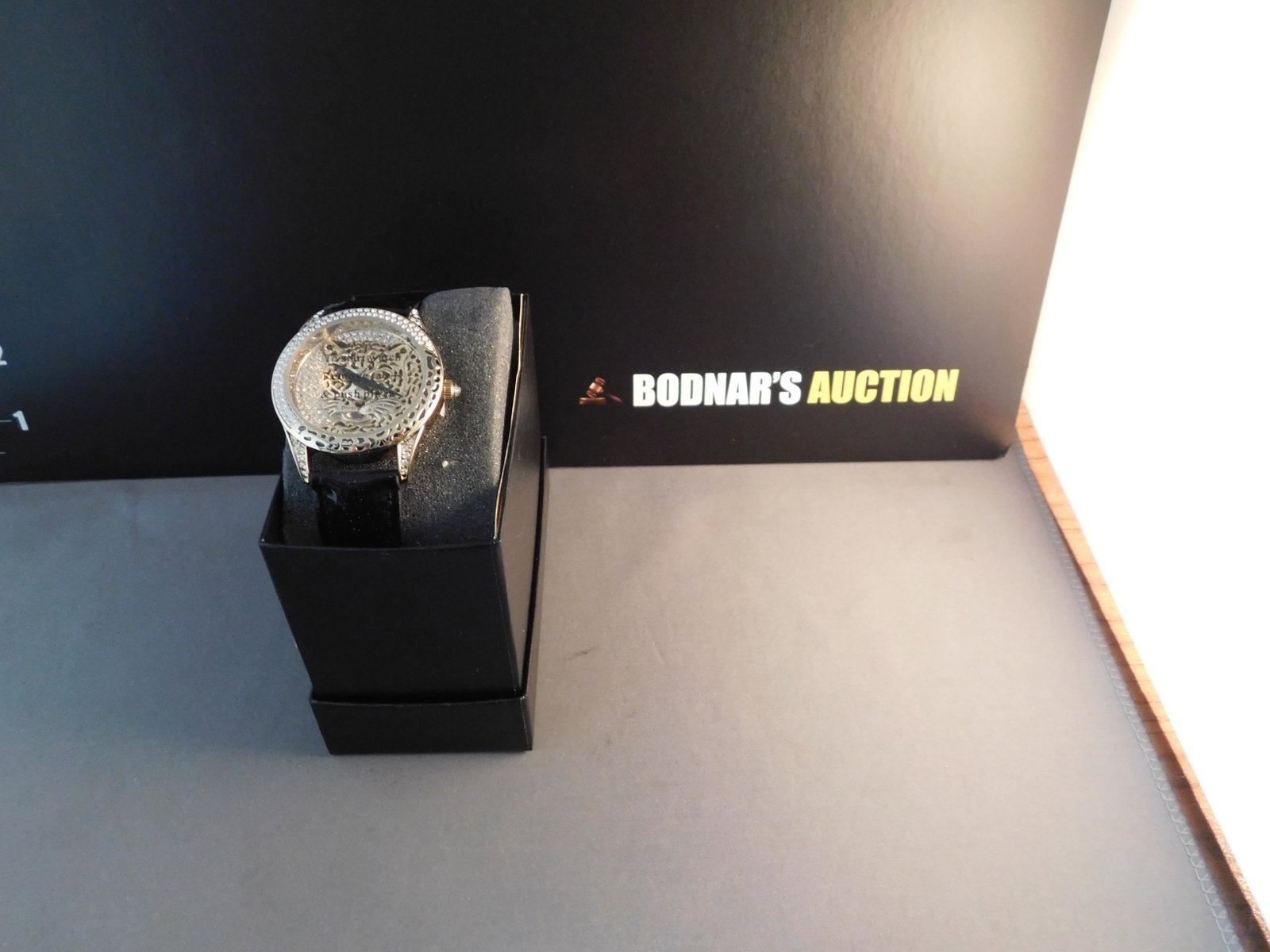 Adrienne Panther Watch: Adrienne gold tone & crystal panther watch. Black patent leather band. Total length 9 1/2". You are bidding at a live sale. Please read the terms and conditions. We are offering no contact pick up at 
