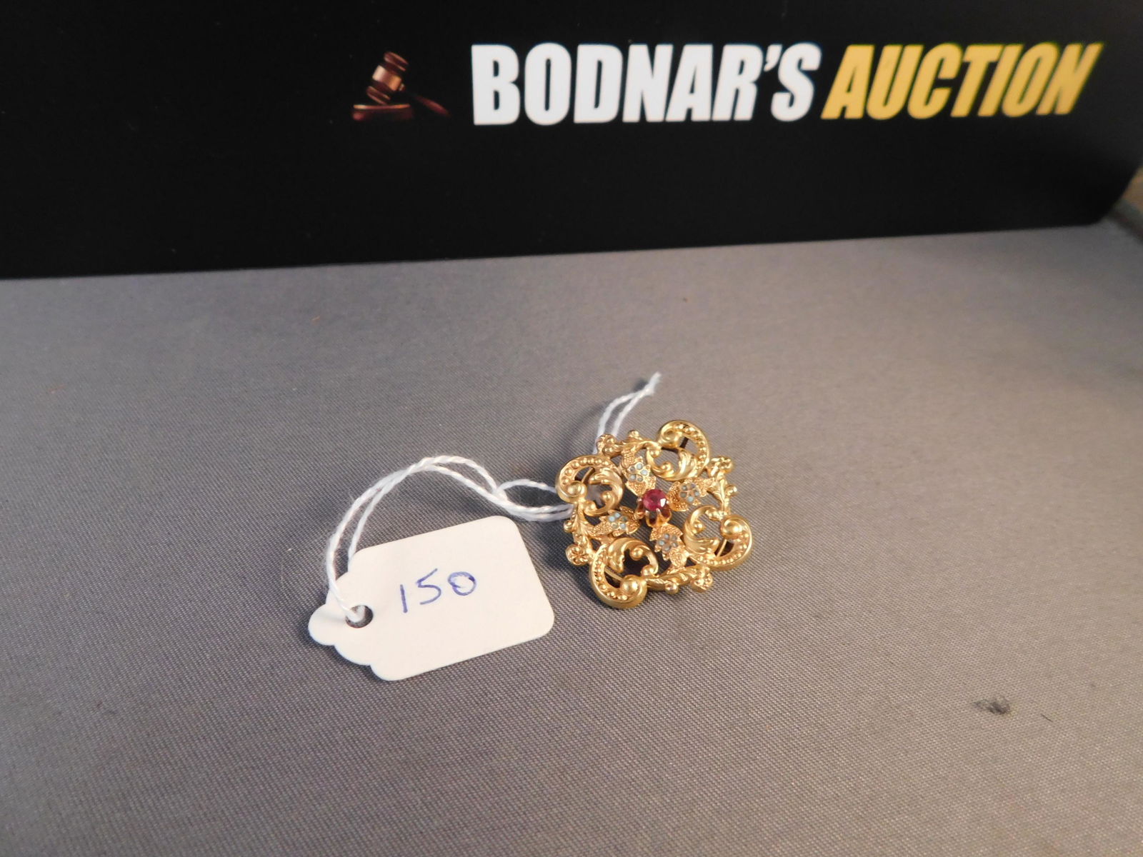 14K Victorian Pin Red Stone: 14K yellow gold pin with red stone. Has turquoise enamel accents. Missing some of the enamel. Marked on clasp 14K. Measures 1". You are bidding at a live sale. Please read the terms and conditions. We