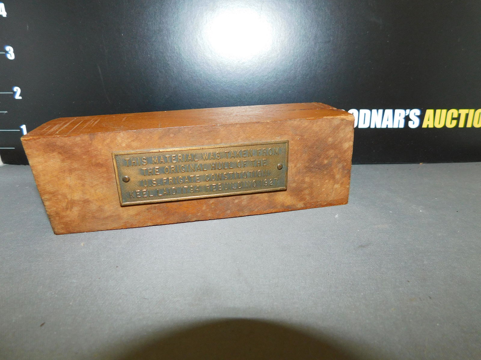 Woodblock Plaque: Woodblock with Plaque that states "THIS MATERIAL WAS TAKEN FROM THE HALL OF THE US FRIGGET CONSTITUTION KEEL LAID 1794 REBUILDING 1927". Measures approx. 2" t x 6" w. You are bidding at a live sale, p