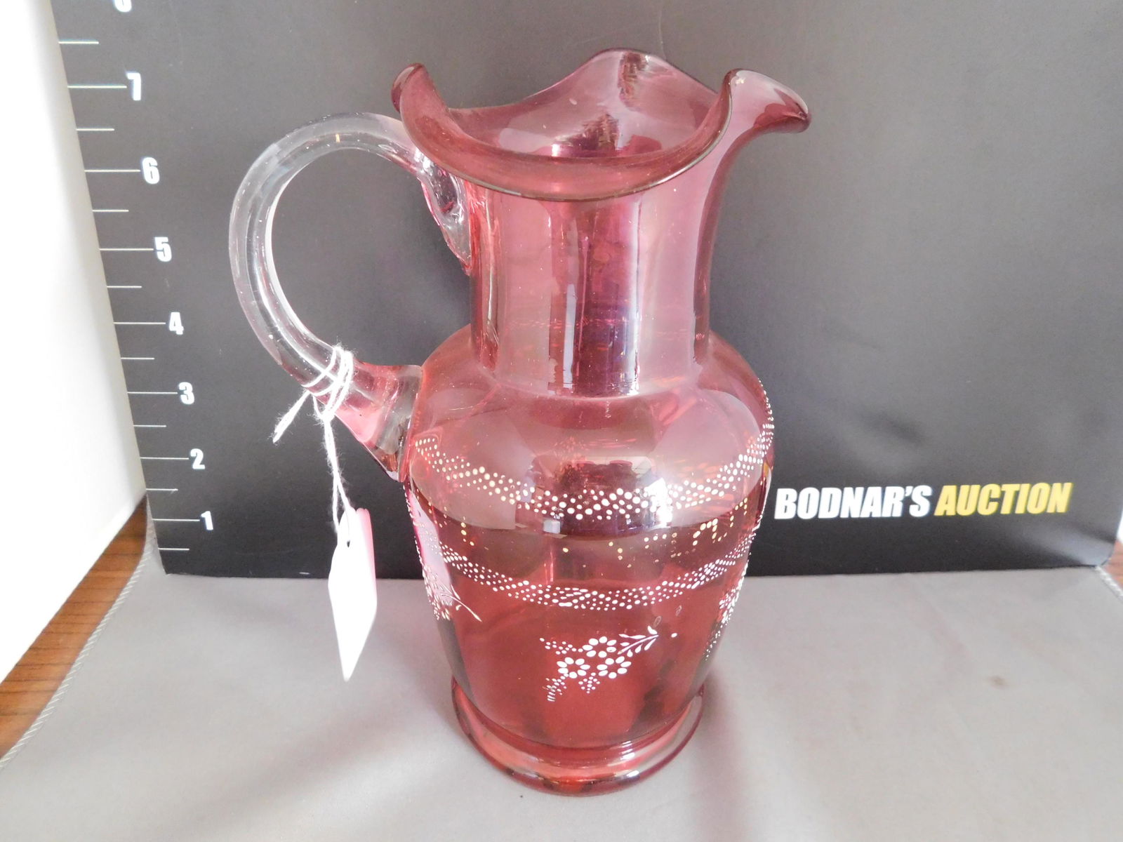 Victorian Cranberry Pitcher: Victorian Cranberry Pitcher. Applied Handle. Enameled Design. Loss to some gold. Measures 8" tall. You are bidding at a live sale, please read the terms and conditions. We are offering contact-less pi