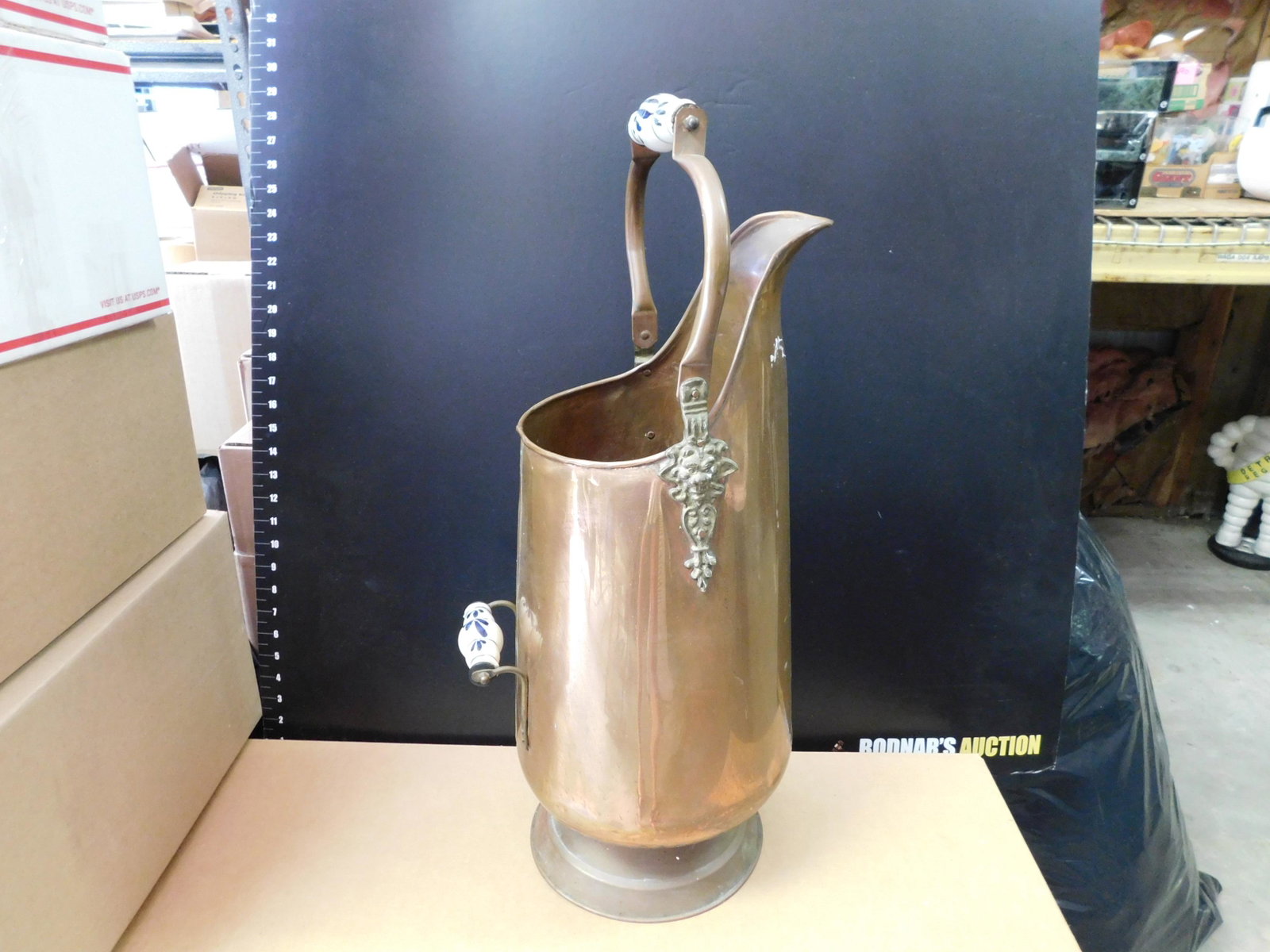 Copper Coal Pot: Large Copper and Brass Coal Pot adorned with Lion Heads with Blue and White Handles. Measures approx. 26" t when handle is up x 10" w. You are bidding at a live sale, please read the terms and conditi