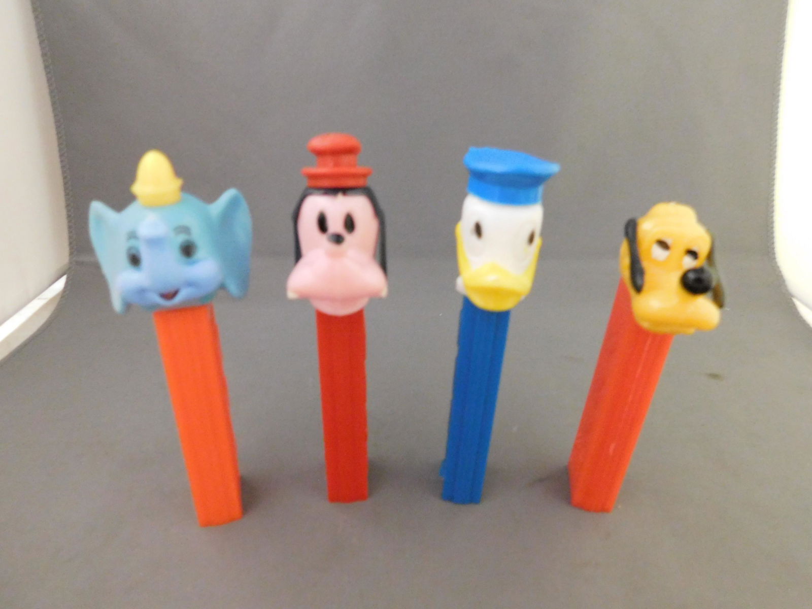 Disney Vintage Pez Lot of 4 - Donald, Pluto, Goofy,: Disney Vintage Pez Lot of 4. They all have no feet. Included in this lot are Donald and Pluto made in Hong Kong and Goofy and Dumbo made in Austria. You are bidding at a live sale, please read the ter