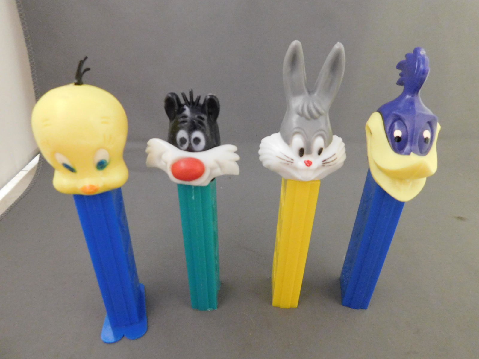 Looney Tunes Vintage Pez Lot of 4: Looney Tunes Vintage Pez Lot of 4. 3 have no feet. Tweety has feet. Included in this lot are Tweety, Sylvester, and Bugs made in Hong Kong and Road Runner made in Austria. You are bidding at a live sa