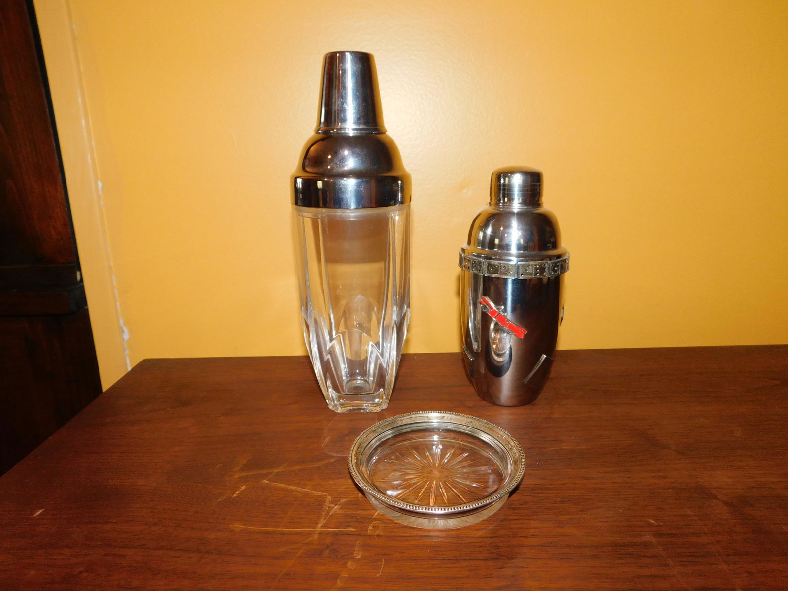 Lot of 2 Cocktail Shakers and Sterling Wine Coaster: Lot of 2 Cocktail Shakers and a Sterling Silver Rimmed Wine Coaster. The tallest shaker measures 11" tall. You are bidding at a live sale, please read the terms and conditions. We are offering contact