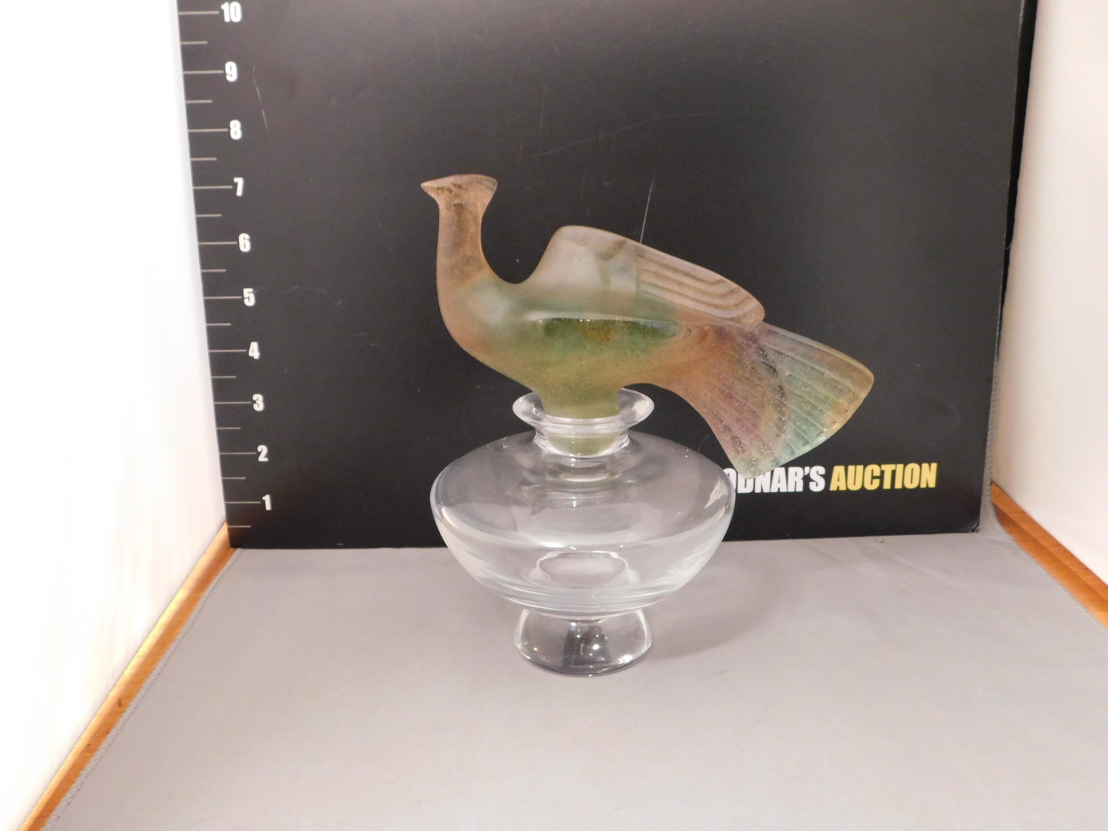 Daum France Bottle With Art Glass Bird Top: Signed Daum France bottle with a pink/green bird topper in a matte glass. Measures approx. 7 1/2" tall x 7" wide. You are bidding at a live sale, please read the terms and conditions. We are offering 