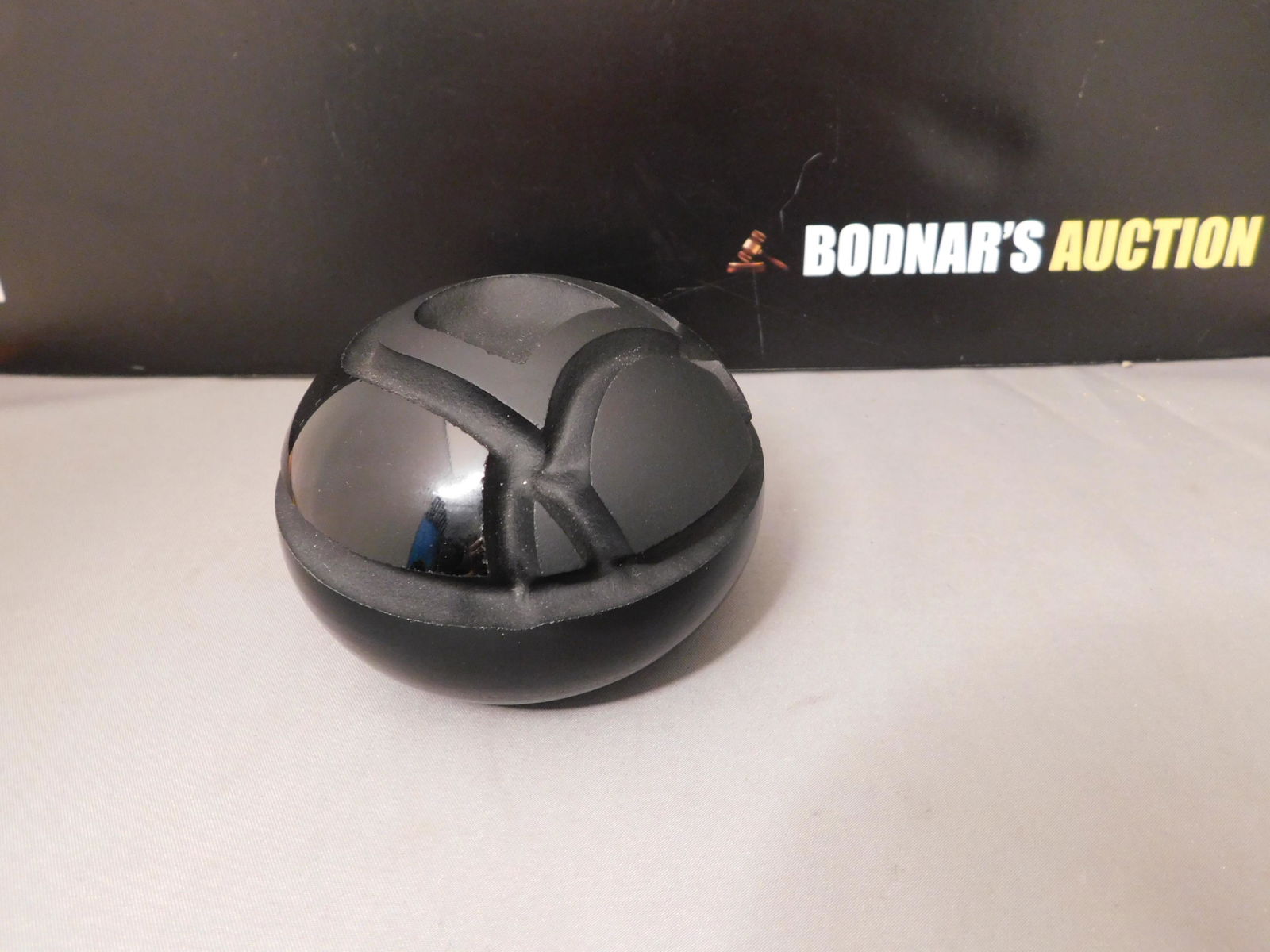 John Gilmor Art Glass Paperweight: Signed John Gilmor art glass paperweight in black glass with frosted accents. Measures approx. 2" tall x 3 1/2" wide. You are bidding at a live sale, please read the terms and conditions. We are offer