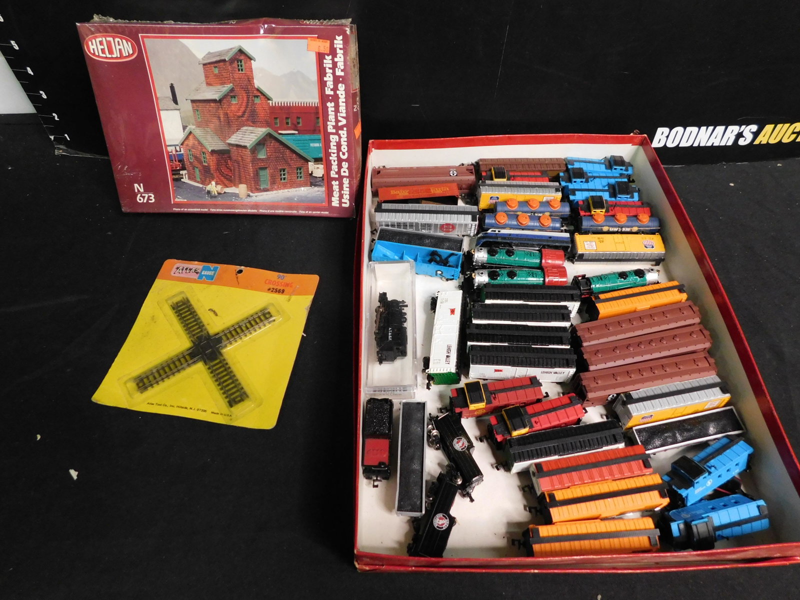 Group Lot of N Scale Trains and Engines: Group Lot of N Scale including 36 Pieces of Rolling Stock, 4 Steam Engines, 1 Diesel Engine, 90 Degree Crossing Track and Heljam Meat Packing Plant Sealed in Box. You are bidding at a live sale, pleas