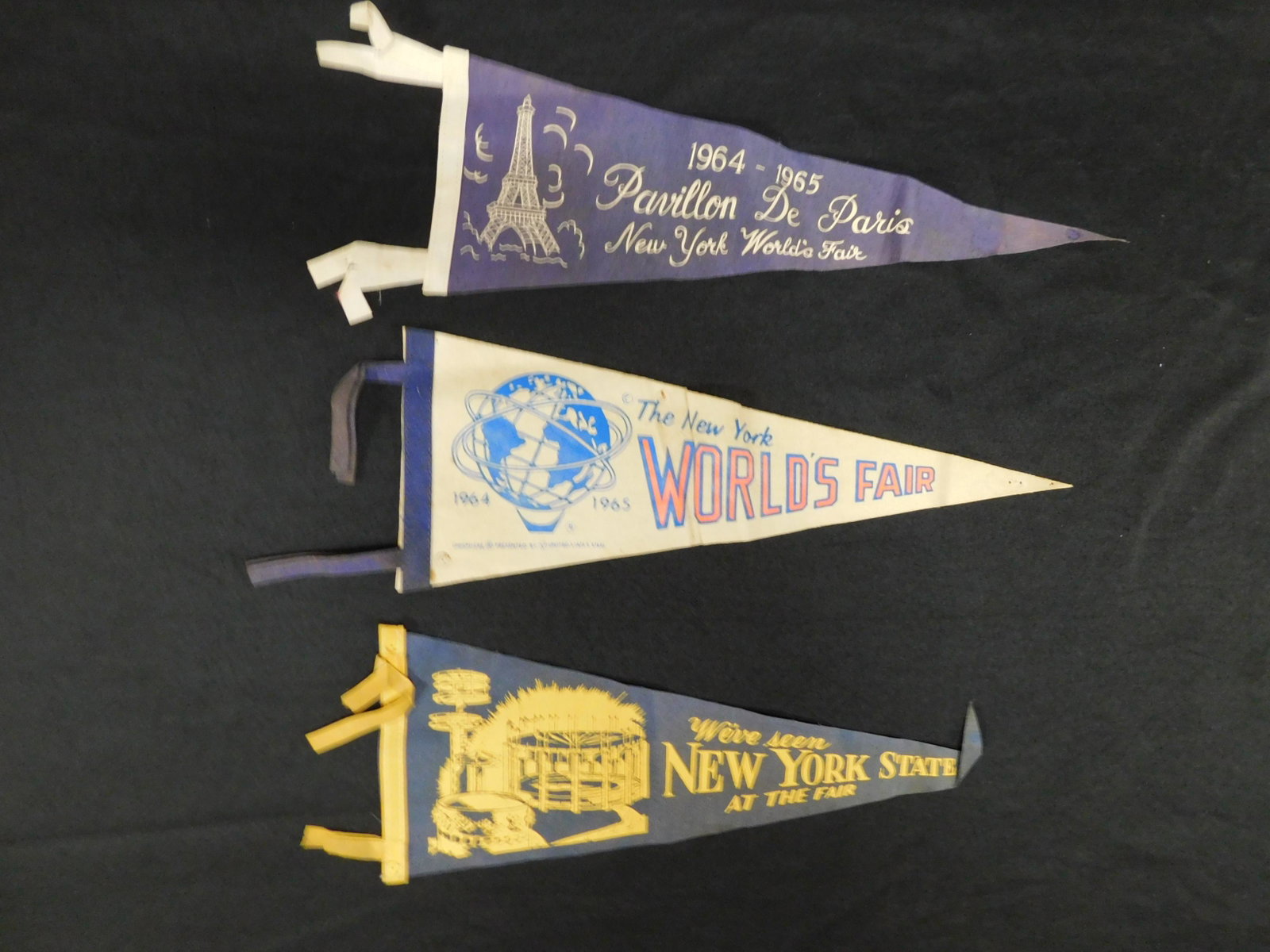 1964 World's Fair Mini Pennant Lot of 3: 1964 World's Fair Mini Pennant Lot of 3. Measures 17.5" long. All have some wear. This sale will be broadcast live on sale day with an auctioneer and caller calling full descriptions of each lot being