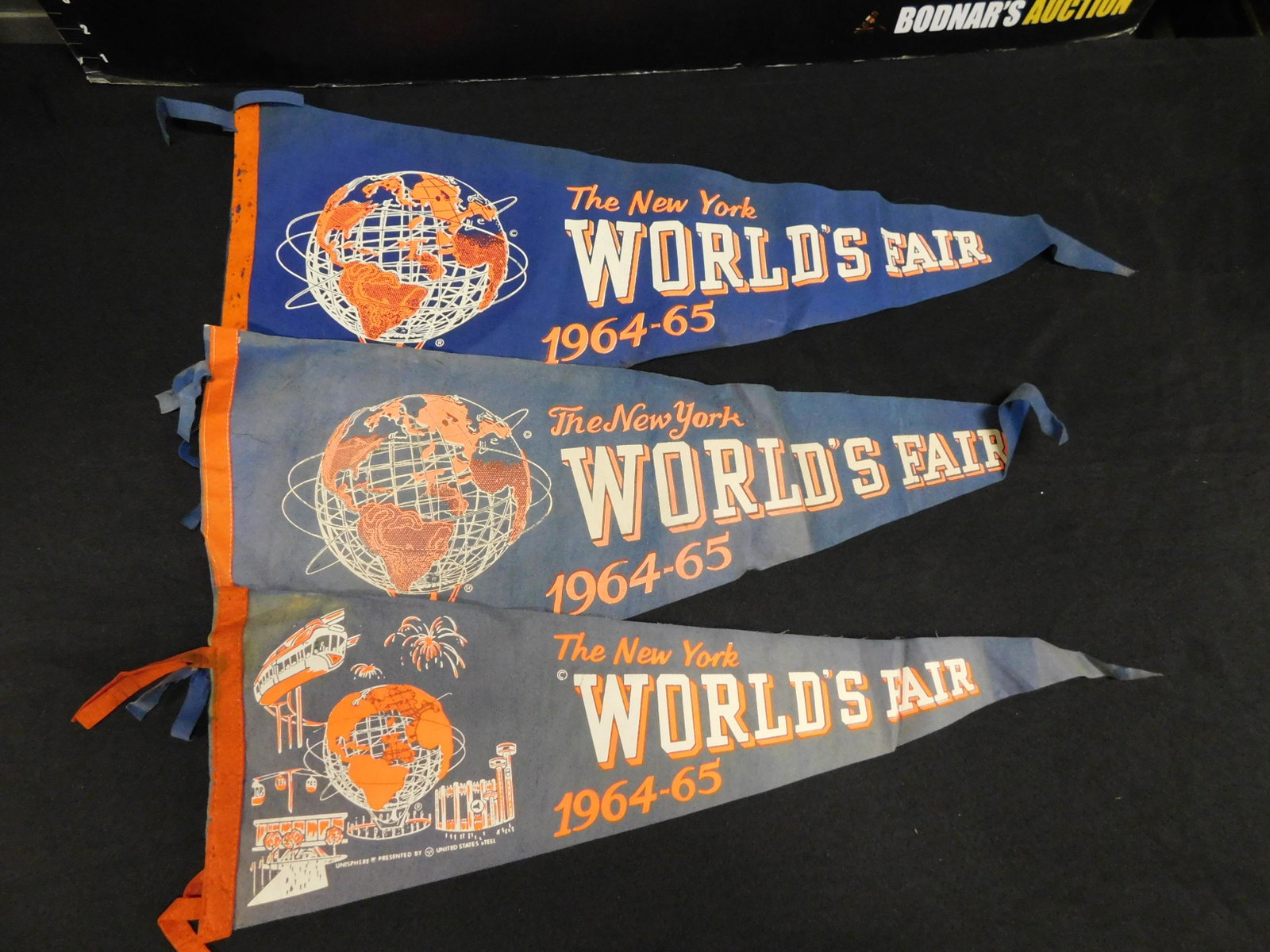1965 World's Fair Pennant Lot of 3: 1964 World's Fair Pennant Lot of 3. They measures approx. 25" long. All have some wear. This sale will be broadcast live on sale day with an auctioneer and caller calling full descriptions of each lot