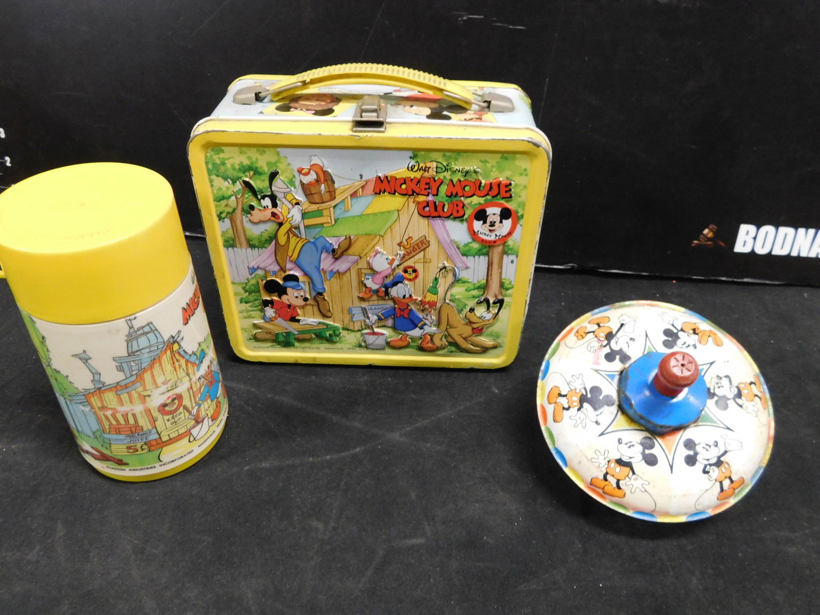 Lot of 2 Vintage Disney Items including Lunchbox with: Vintage Mickey Mouse Club by Aladdin Metal Lunchbox with Thermos 1976 and a Vintage 1975 Walt Disney Productions Mickey Mouse Top. This sale will be broadcast live on sale day with an auctioneer and c