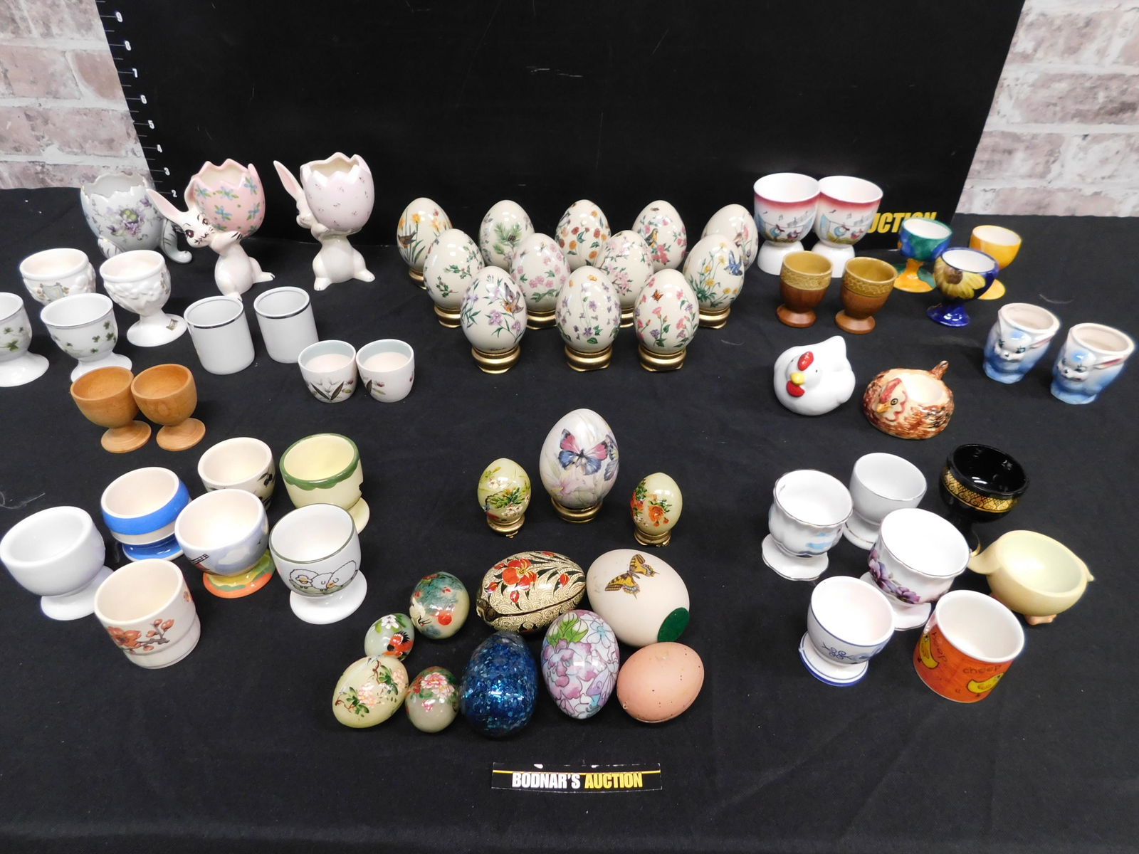 Box Lot of Egg Cups and Porcelain Eggs: Box Lot of Egg Cups and Porcelain Eggs including the Lenox. This sale will be broadcast live on sale day with an auctioneer and caller calling full descriptions of each lot being sold, as well as vide
