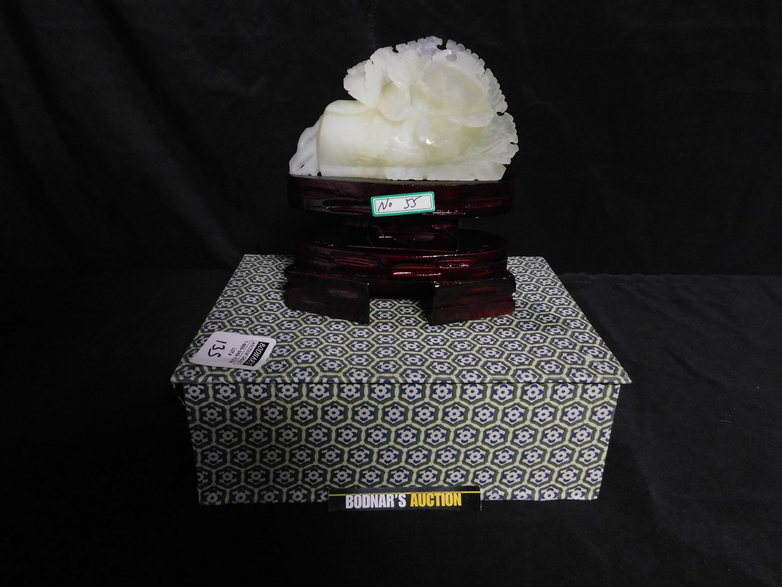 Carved Stone of Flowers on Wooden Base: Carved Hard Stone - Possibly Jade - Flowers on Wooden Base. Measures 8" tall x 6" long when on base. Stone measures 5". You are bidding at a live sale, please read the terms and conditions. We are off