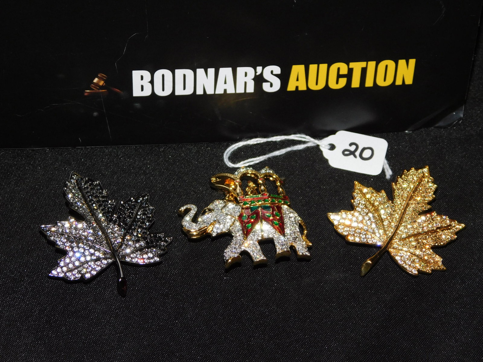 3 Kenneth Jay Lane Pins: 3 Kenneth Jay Lane pins including a leaf pin in a gold tone and rhinestone, a leaf pin in a gun metal tone with rhinestones and an elephant pin in a gold tone with rhinestones. Measures approx. 2 1/2"