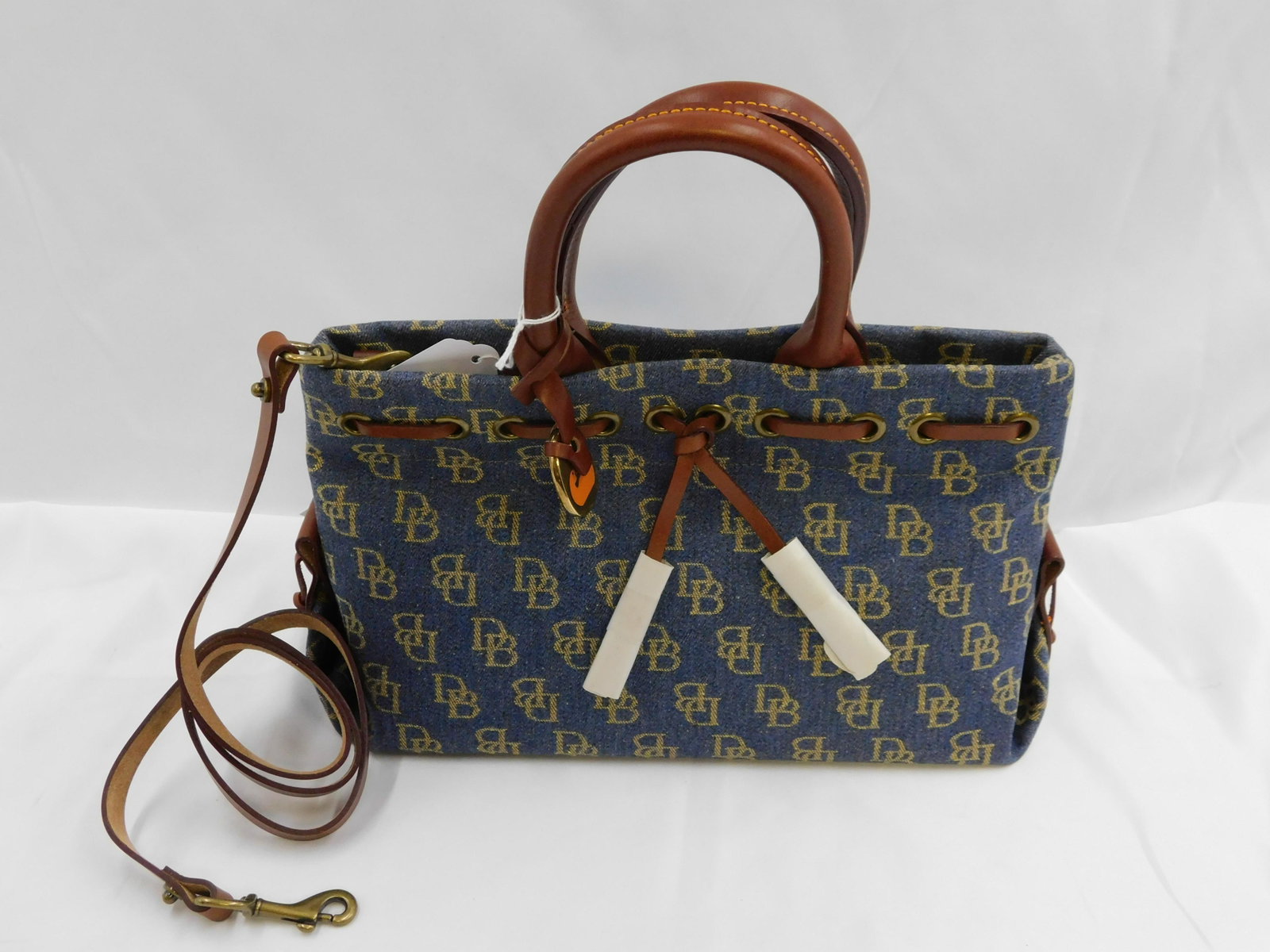 Dooney & Burke Brown Tassel Tote: Dooney & Burke Brown Tassel Tote. In Blue Cloth with Brown Leather Accents. Tissue paper has left residue on inside handle. Includes Longer Strap. Measures 12" wide x 11.5" tall. New with Tag. Removed