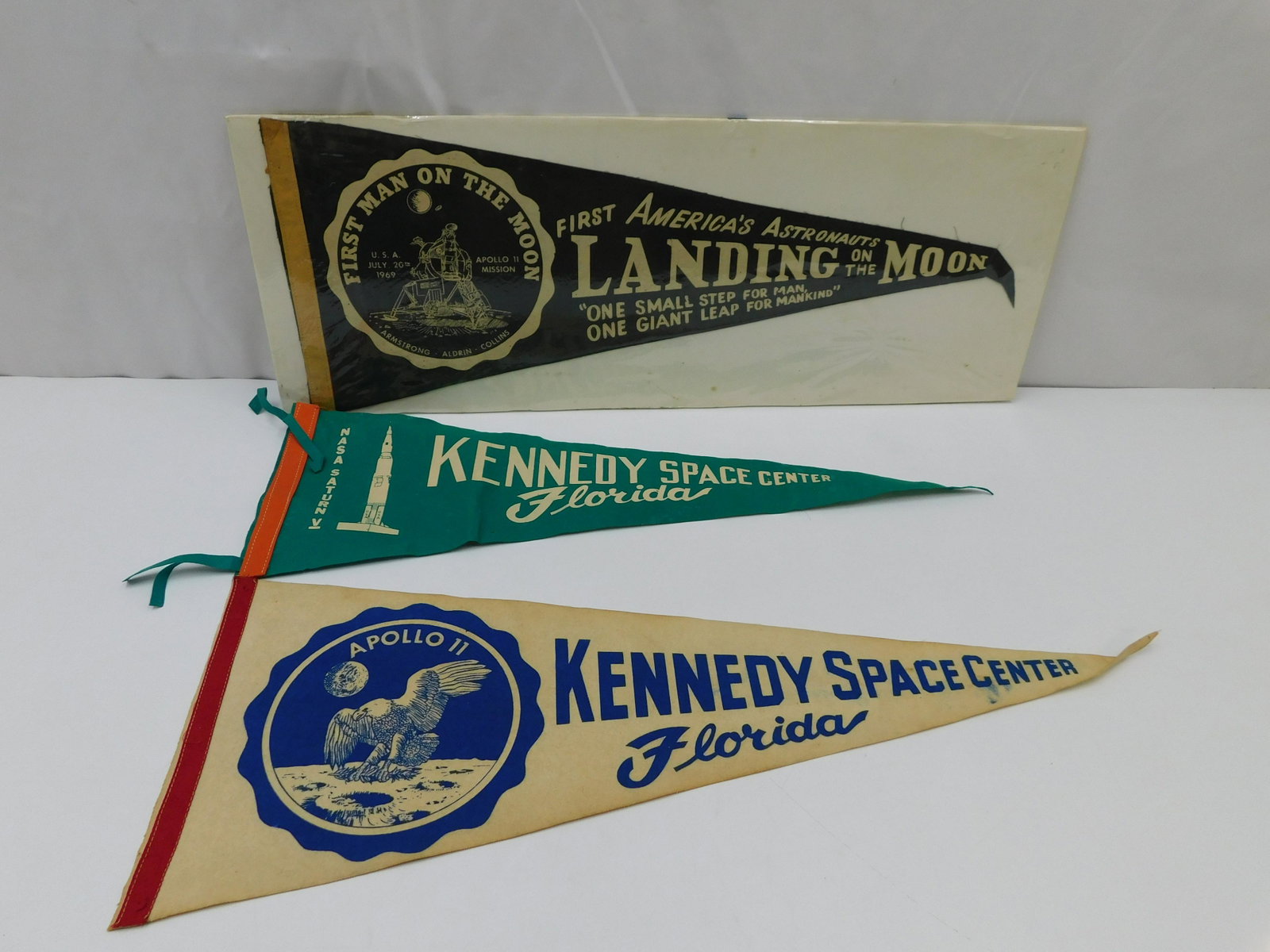 Lot of 3 NASA Pennants: Lot of 3 NASA Pennants including (2) Kennedy Space Center - One from Saturn 5 and other from Apollo 11 and 1st Man on the Moon Pennant. All in good condition. Two are missing tie on's. Measures approx