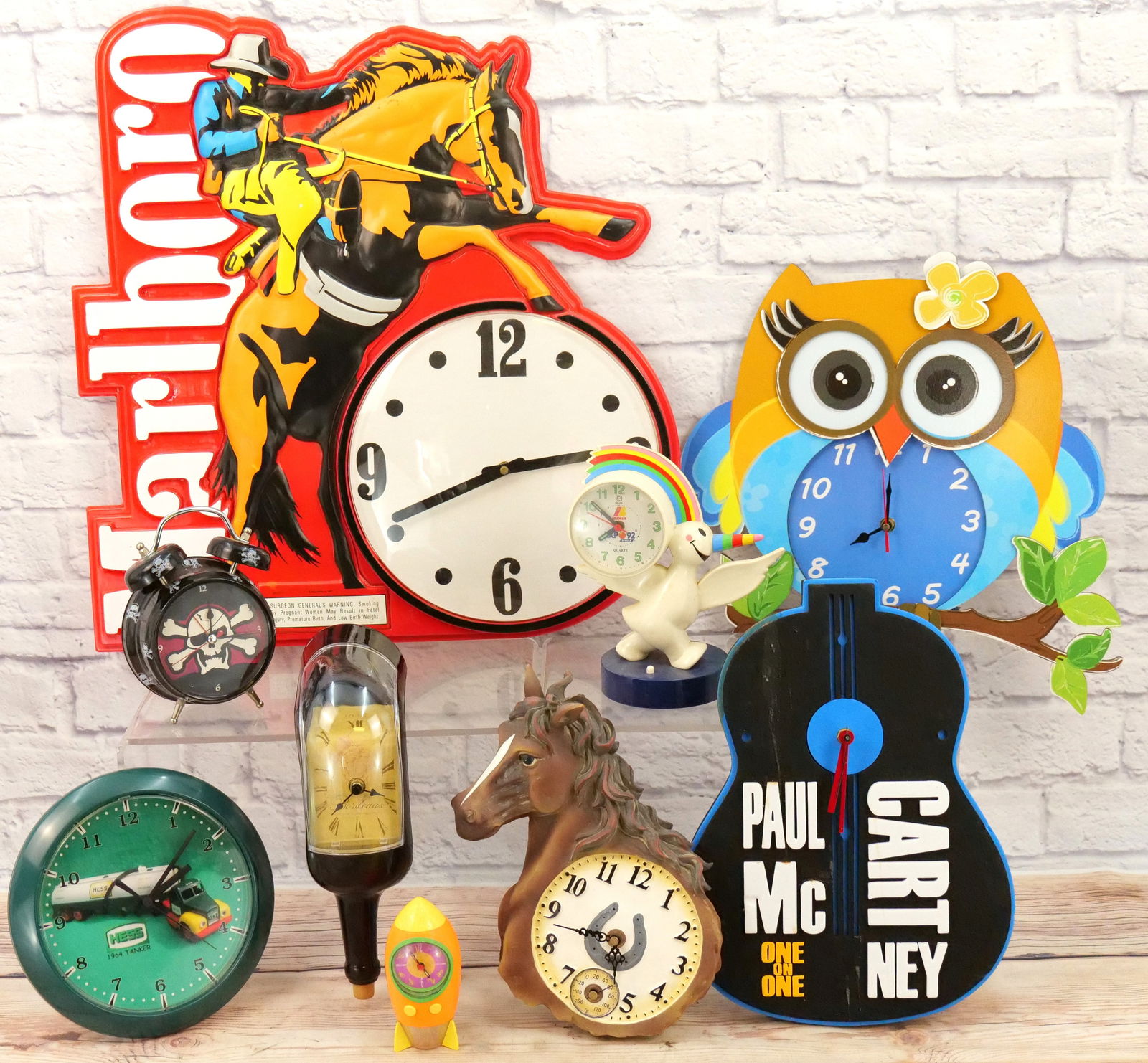 Lot of 9 Novelty Clocks: Lot of 9 Novelty Clocks including Marlboro Advertising, Paul McCarthy Foam Guitar Shaped Clock, Louis Bordeaux Hanging Shelf Wine Bottle Clock, Rocket Ship Clock, Iberia Expo Unicorn Clock, Skull Cloc