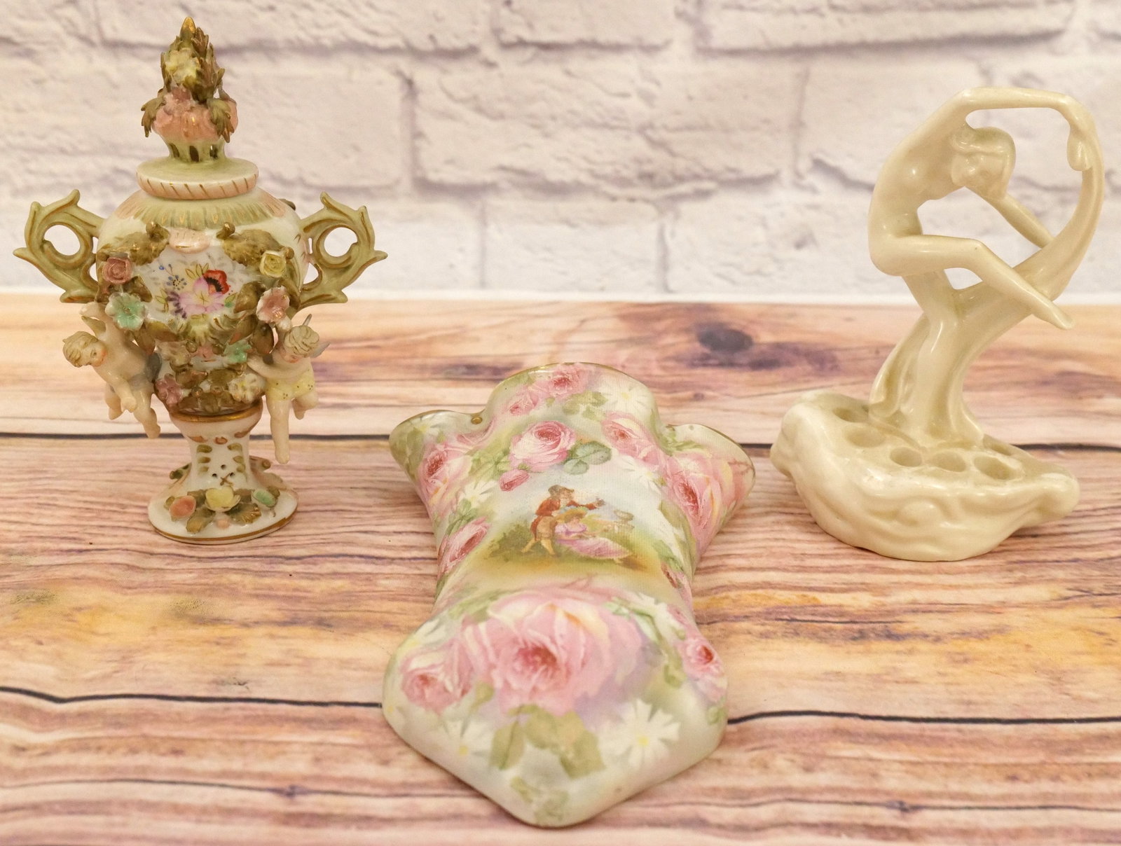 Lot of 3 Decorative Items: Group Lot of 3 Decorative Items including Royal Bayreuth Rose Tapestry Wall Pocket, Porcelain Covered Urn with Cherubs - All flowers intact, and Art Nouveau Nude Flower Frog. Largest measures 9" tall.