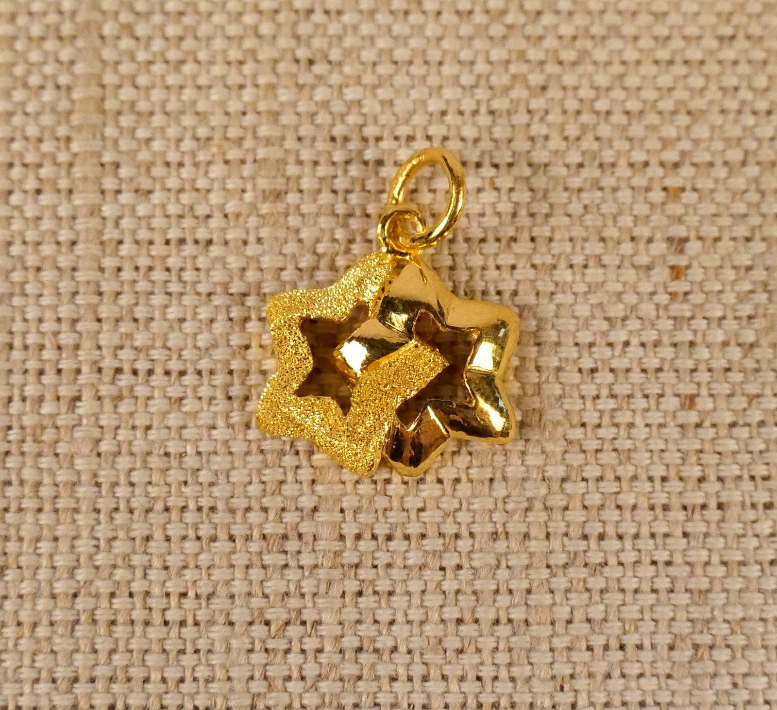 24K Yellow Gold Star Pendant: 24K Yellow Gold Star Pendant. 24K yellow gold pendant featuring 2 intertwined stars (1 high polish, 1 textured). It measures .80'' x .58'' and Weighs approx. 2.6 grams. All invoices must be paid withi