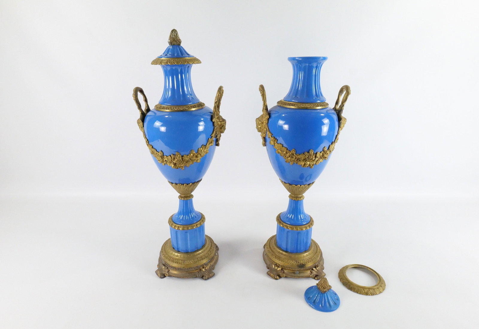 Pair of Sevres Style Double Handled Urns: Pair of Sevres Style Decorative Double Handled Urns with Bronze Mounts. Top Bronze Mount on one Urn needs to be reattached. Otherwise very good condition. Measures 26" tall x 9.5" diameter. All invoic