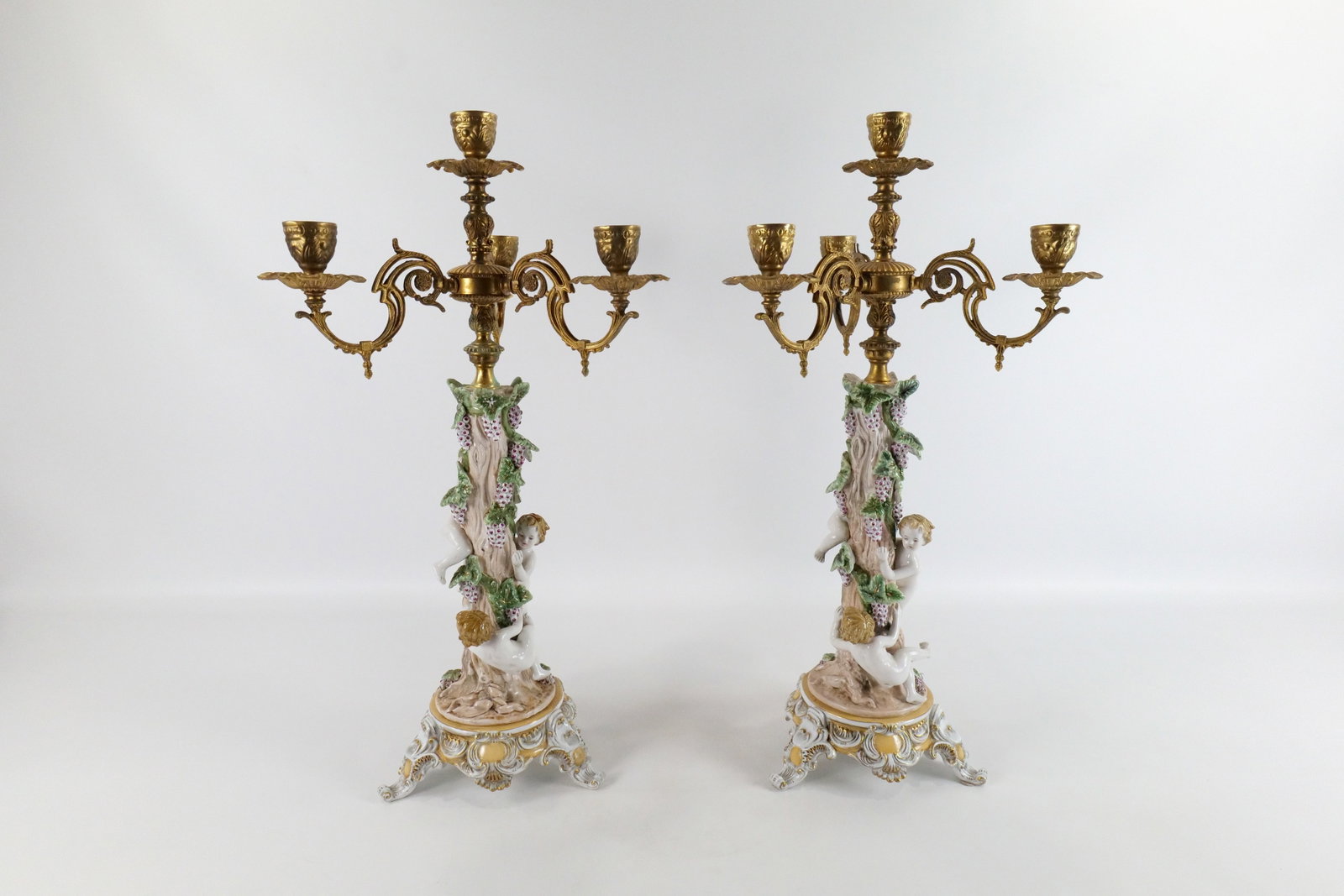 Pair of Porcelain and Brass Decorative Candelabras: Pair of Porcelain and Brass Decorative Candelabras. Depicting Cherubs Picking Grapes. Bears cross sword marks. Good Condition. Measures 27" tall x 13.5" wide. All invoices must be paid within 24 hours