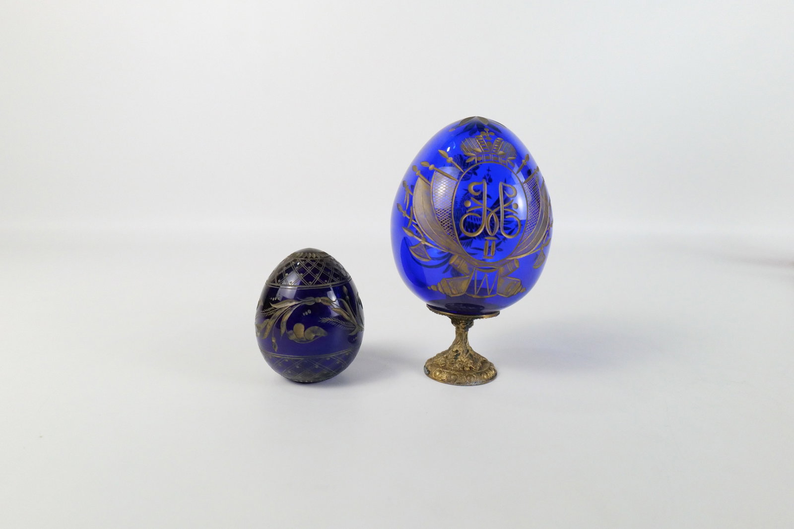 Lot of 2 Russian Faberge Style Engraved Glass Eggs: Lot of 2 Russian Faberge Style Engraved Glass Eggs. One has Russian Coat of Arms and Other has Flower Leaf Design. Smaller one signed on bottom. Other has Paper Label - Made in Russia. Largest measure