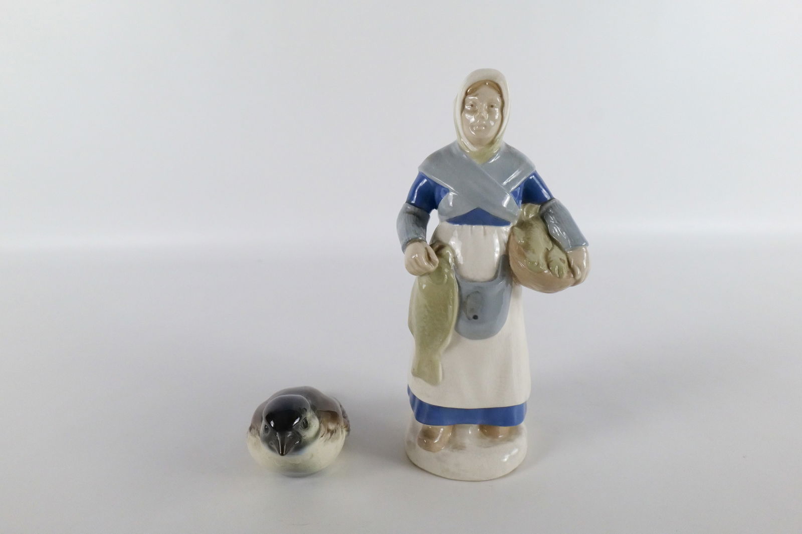 Lot of 2 German Porcelain Figurines: Lot of 2 German Porcelain Figurines including Lippelsdorf Woman with Fish and Goebel Bird. Crazing present but overall good condition. Largest measures 8.25" tall. All invoices must be paid within 24
