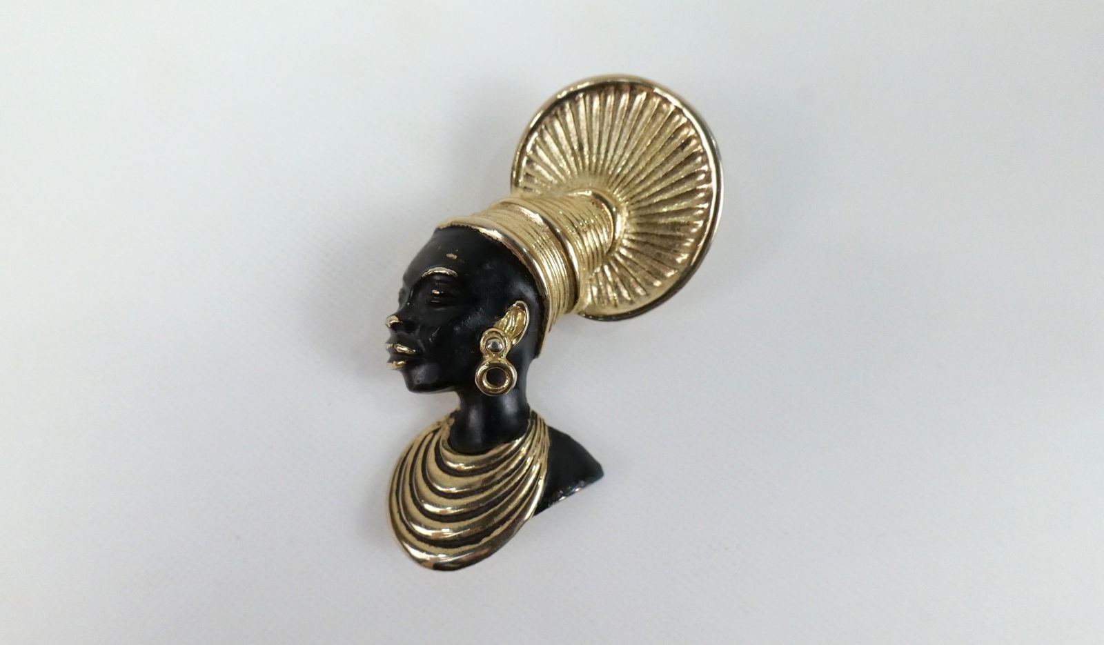 Vintage Zulu Woman Brooch by Coro: Vintage Zulu Woman Brooch by Coro. The lot includes 1 vintage c1950 gold tone brooch of a African Zulu woman by Coro measuring 2.62'' x 1.43'' with black painted accents. Marked Coro, used. All invoic