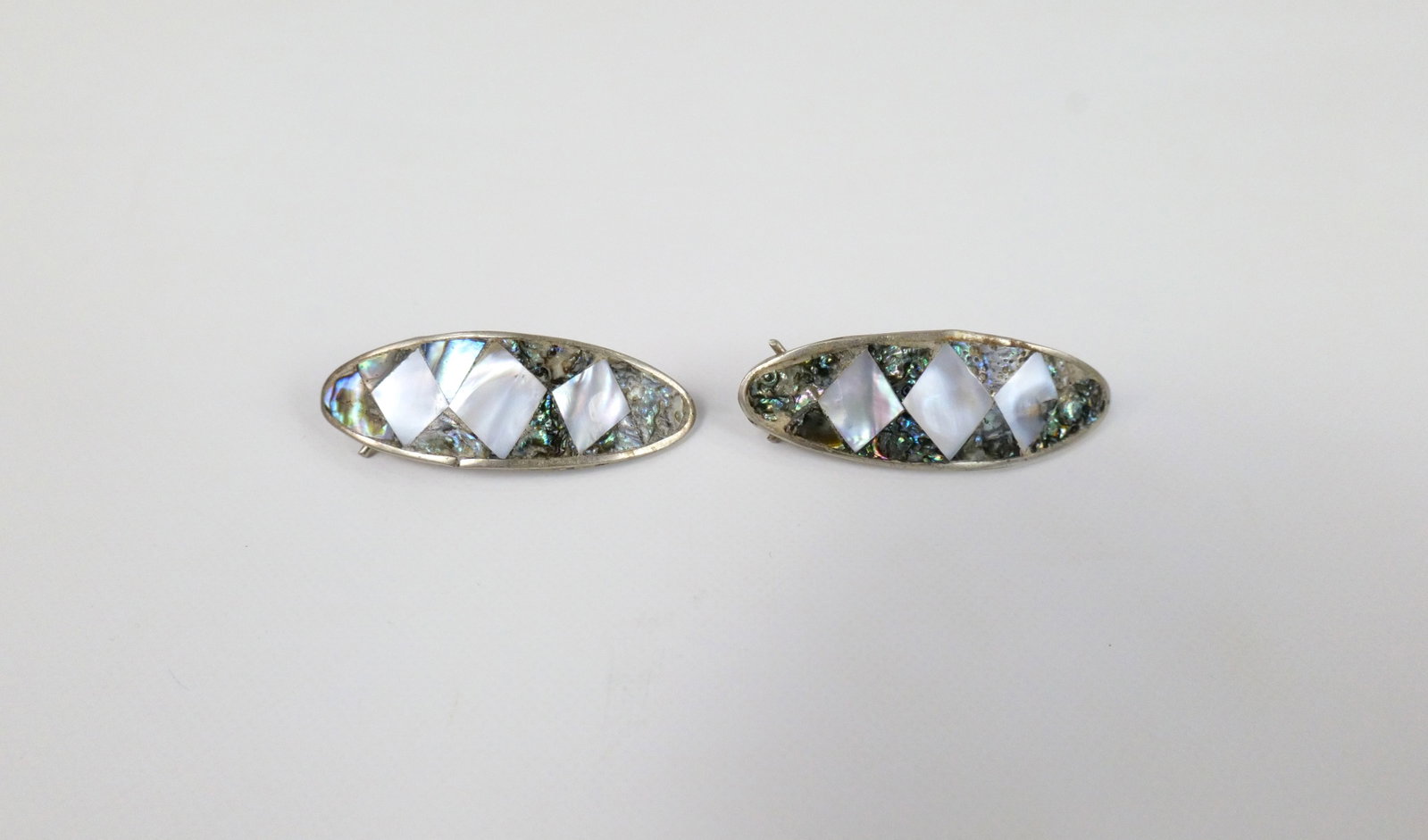 Pair of Mexican Made Inlaid Barretts: Pair of Mexican Made Inlaid Barretts. The lot includes 1 vintage pair of silver Mexican made elontated oval barrettes measuring 2'' x 3/4''and featuring abalone and mother of pearl inlays. Marked Mexi