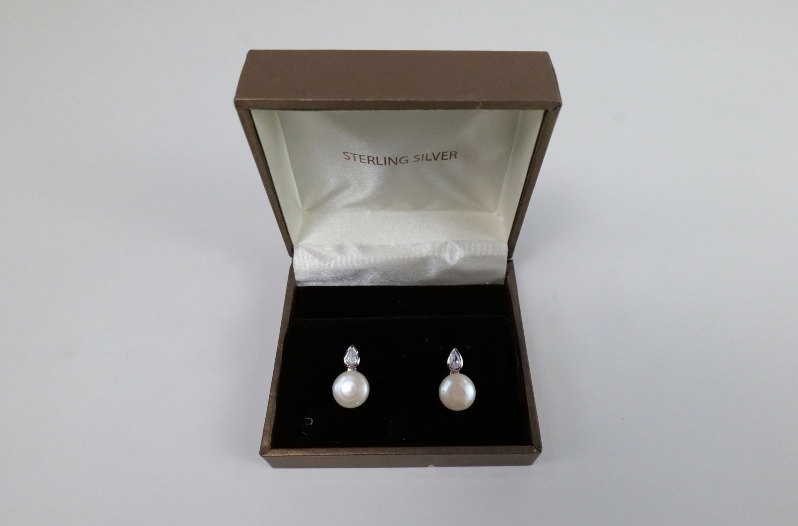 CZ and Freshwater Pearl Stud Earrings: CZ and Freshwater Pearl Stud Earrings. The lot includes a pair of .68'' long sterling stud earrings featuring a pear shaped 5mm x 4mm CZ with a 10mm white disc freshwater pearls. Marked 925 Thailand,