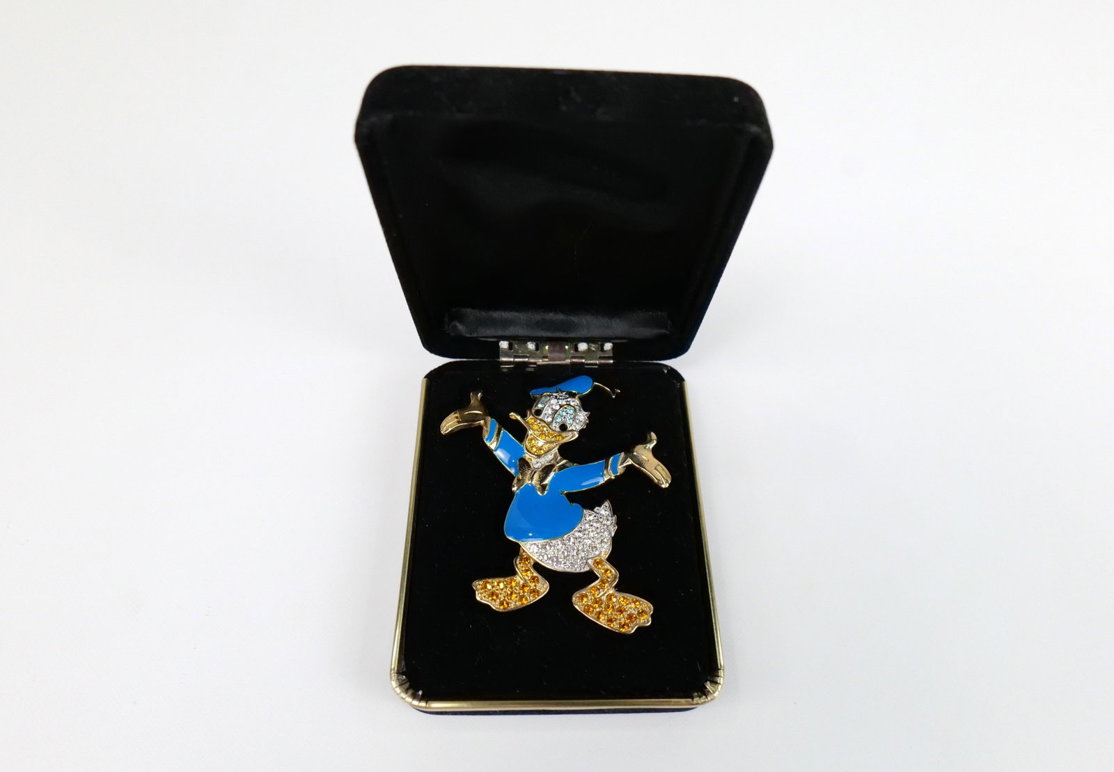 Vintage Donald Duck Rhinestone Brooch: Vintage Donald Duck Rhinestone Brooch. The lot includes a 3'' x 2 3/4'' vintage gold tone Donald Duck brooch by Disney featuring blue/black enamel clothing and multicolored rhinestone accents. Marked 