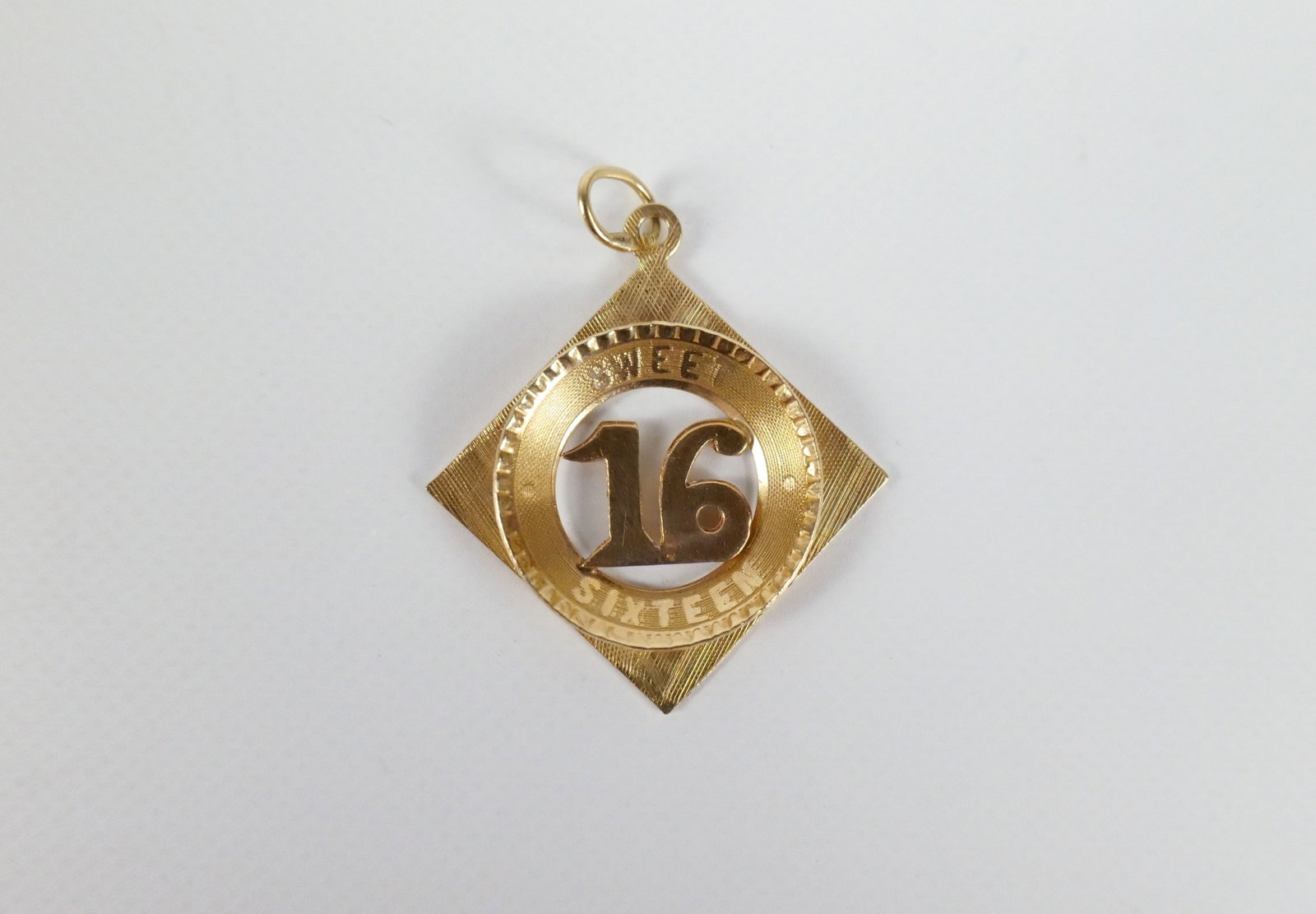 Vintage 14K Sweet 16 Charm: Vintage 14K Sweet 16 Charm. The lot includes a vintage mid century 14K 1.15'' x 1.04'' square charm set on point with a pierced work 16 at the center in a convex circular frame with the phrase Sweet S