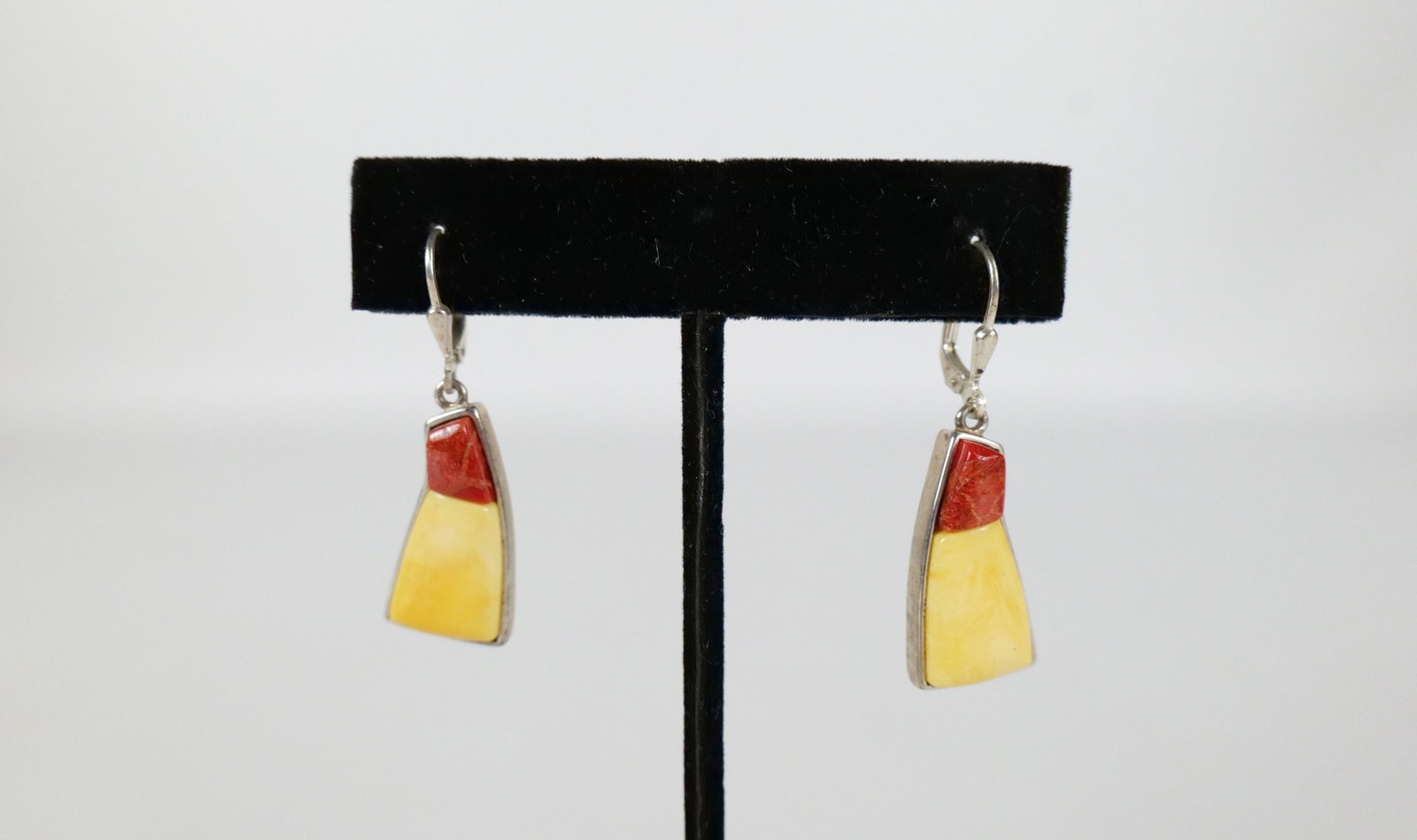 Pair of Amber/Coral Sterling Earrings: Pair of Amber/Coral Sterling Earrings. The lot includes a pair of 1.5'' x .48'' tapered rectangular earrings with sterling frames featuring both creamy butterscotch amber and red coral cabochons with 