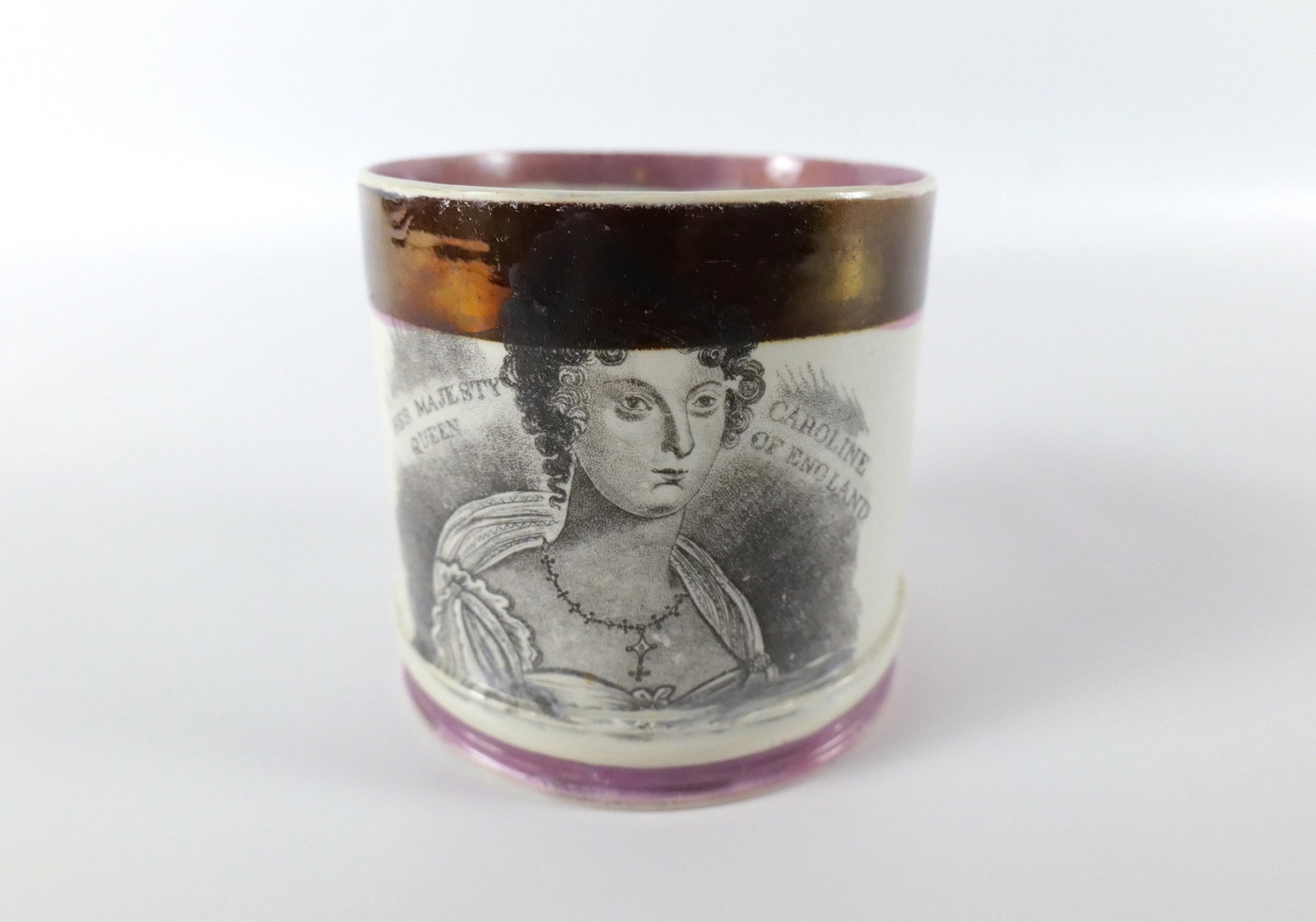 Her Majesty Queen Caroline Mug: Her Majesty Queen Caroline mug done in a white pottery with a black transfer image of Caroline and working above and a large luster trim at the top and a purple band at the base (the purple paint has 