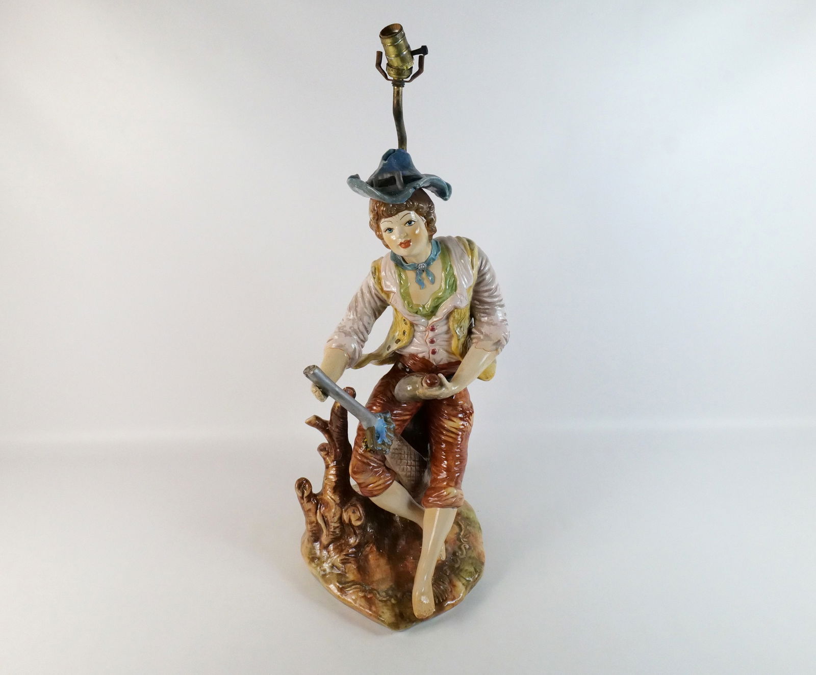 Capodimonte Figural Table Lamp: Capodimonte Figural Table Lamp. Depicting a Young Man with a Shotgun and Some Booze. Some chipping present. Measures 32" tall x 16" wide. All invoices must be paid within 24 hours of the sale. We offe