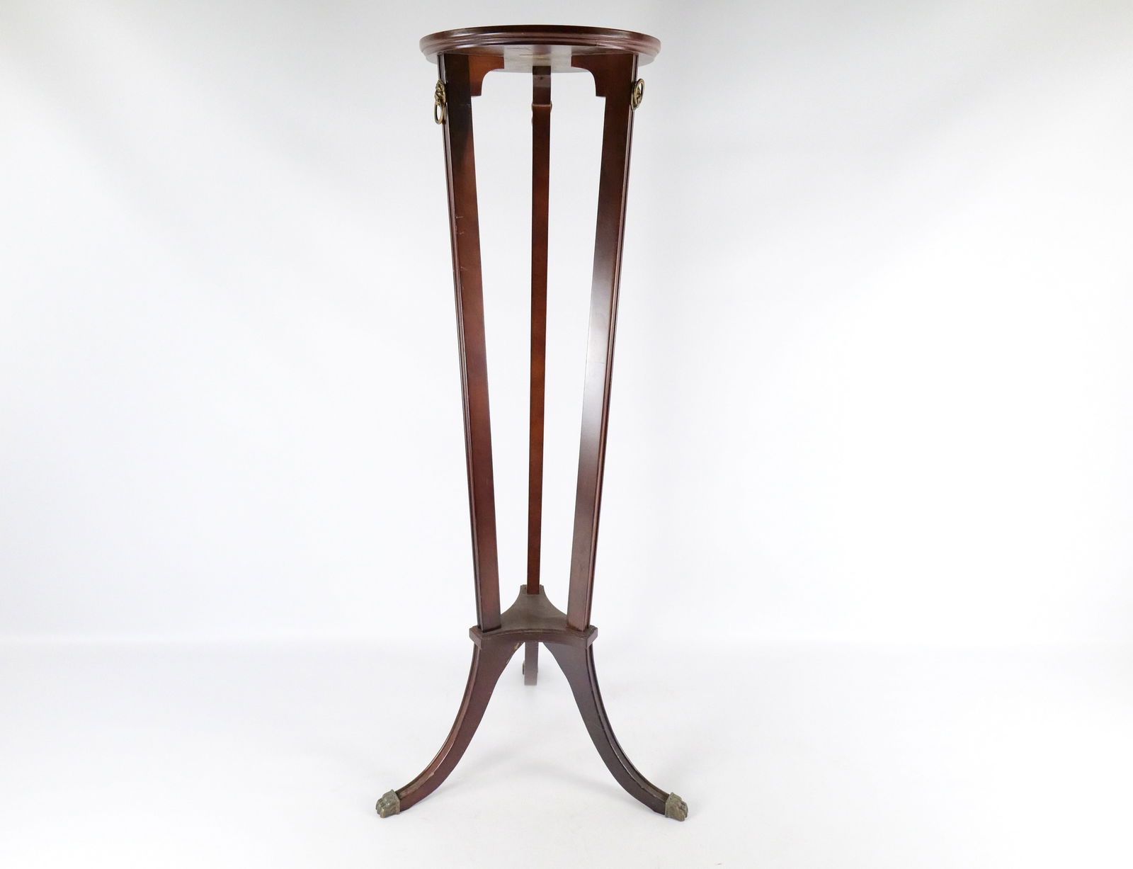 The Bombay Company Mahogany Wood Plant Stand: The Bombay Company Mahogany Wood Plant Stand. Has brass accent decoration. Some scratching and scuffing to the wood but overall good condition. Circa Late 20th Century. Measures 40" tall x 17.5" wide.