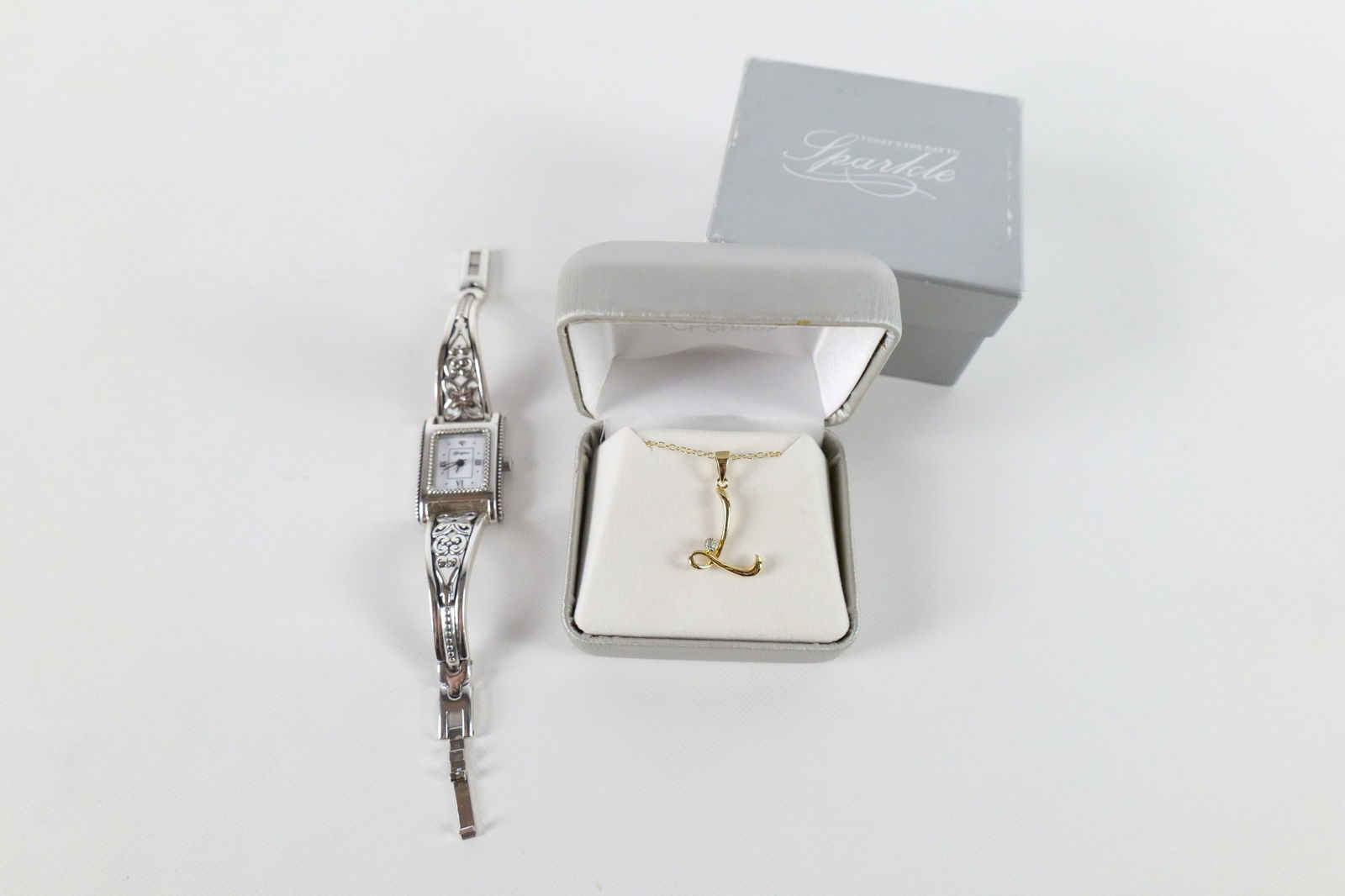 Ladies Brighton Watch and Initial Necklace : Ladies Brighton Watch and Initial Necklace. The lot includes an adjustable silver tone quartz watch by Brighton featuring a .77'' x .83'' rectangular case, a white face, and a decorative bracelet with