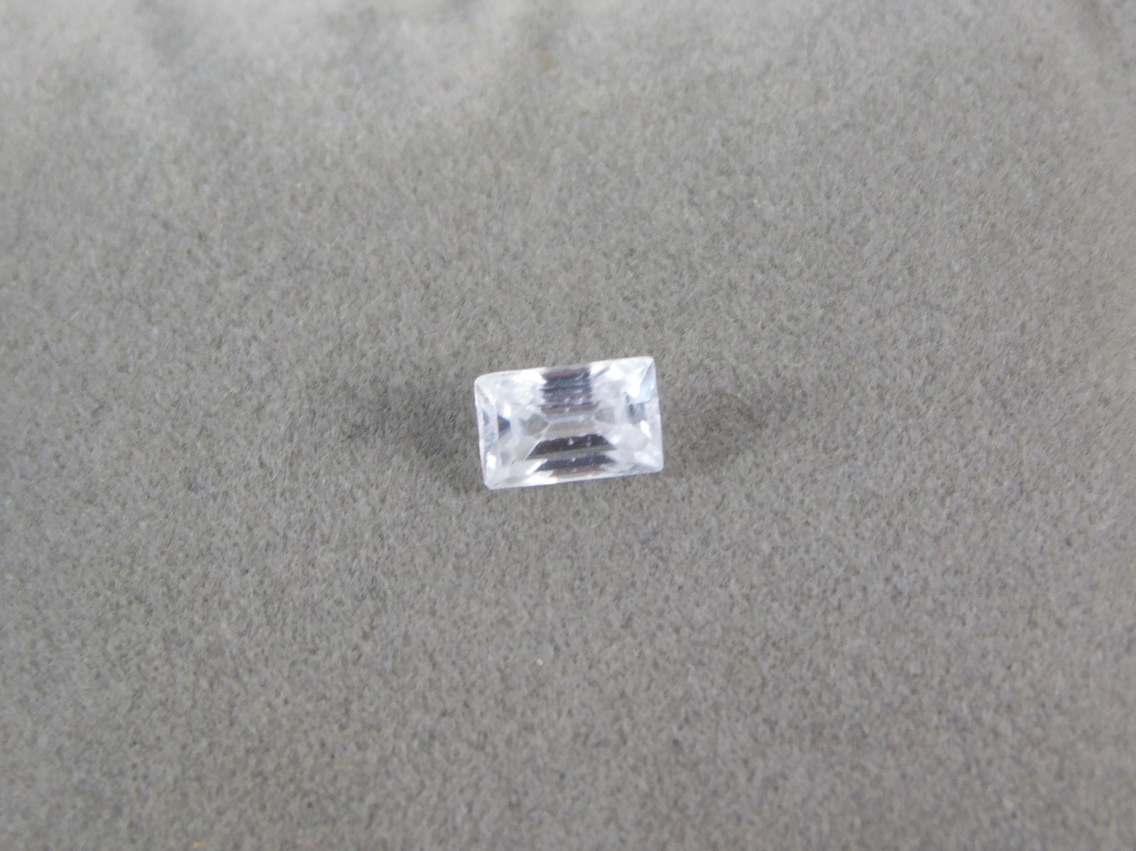 Emerald Cut Natural Diamond : Emerald Cut Natural Diamond. The lot features a 6mm x 4mm x 2.8mm modified emerald cut, colorless natural diamond with noticeable scratches, abrasions, and wear to the facet junctions at 10X magnifica