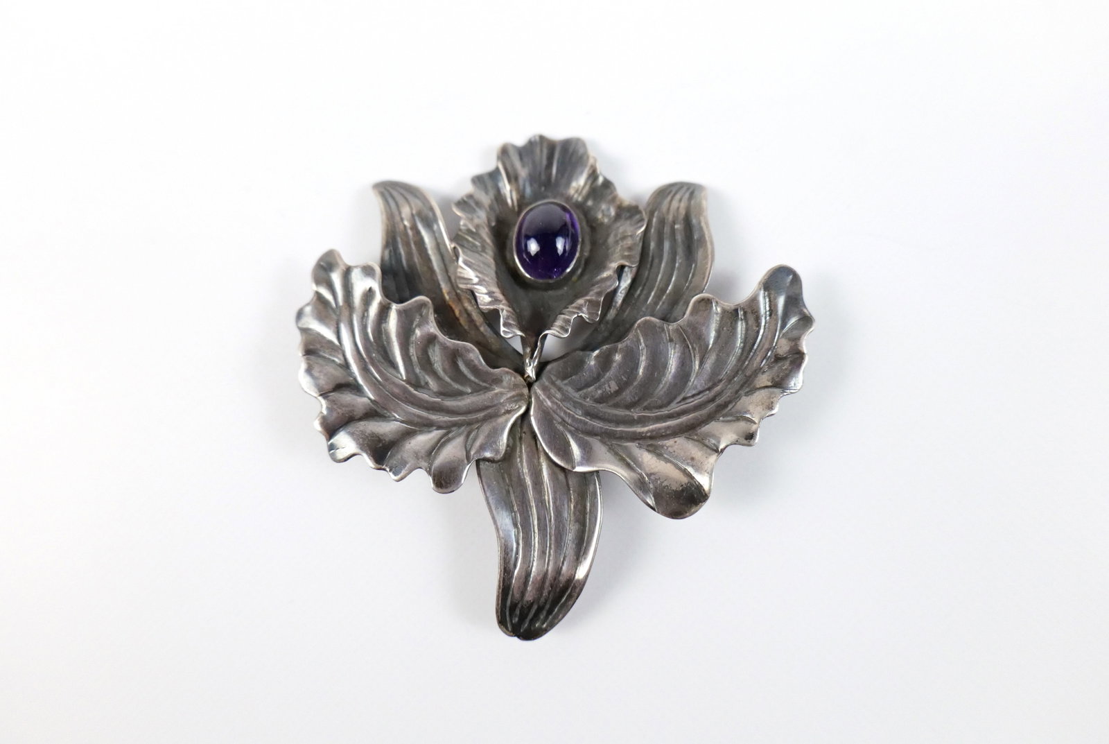 Vintage Sterling Cattaleya Orchid Brooch: Vintage Sterling Cattleya Orchid Brooch. The lot includes a vintage 2.5'' x 2.47'' sterling brooch in the form of a cattleya orchid with a 11mm x 8.8mm oval amethyst cabochon and a hinged bar closure 