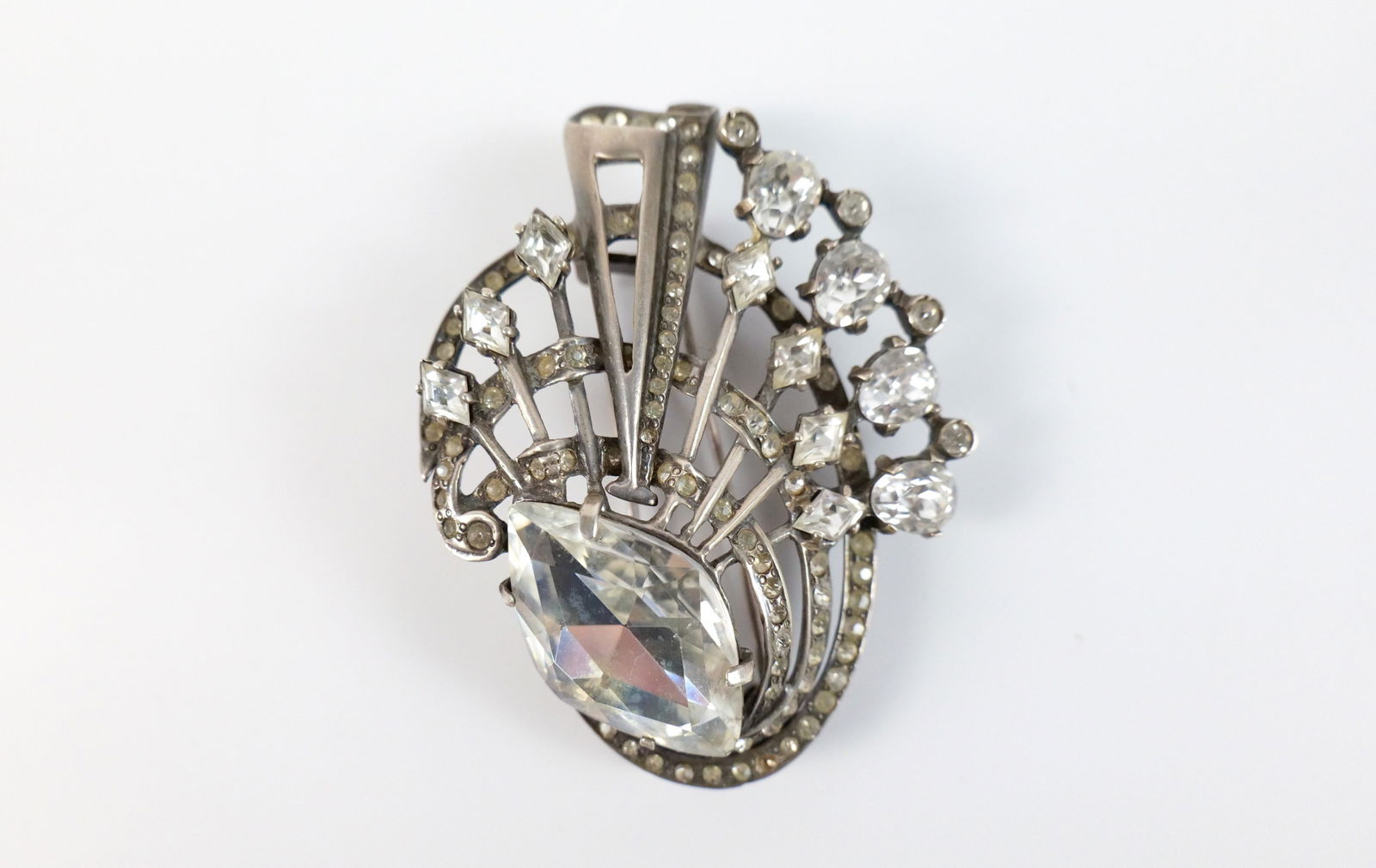 1940s Sterling Eisenburg Fur Clip: 1940s Sterling Eisenburg Fur Clip. The lot includes a vintage 1940s 2.92'' x 2.23'' sterling fur clip in a deco style setting accented with white glass rhinestones and a hinged double bar closure at t