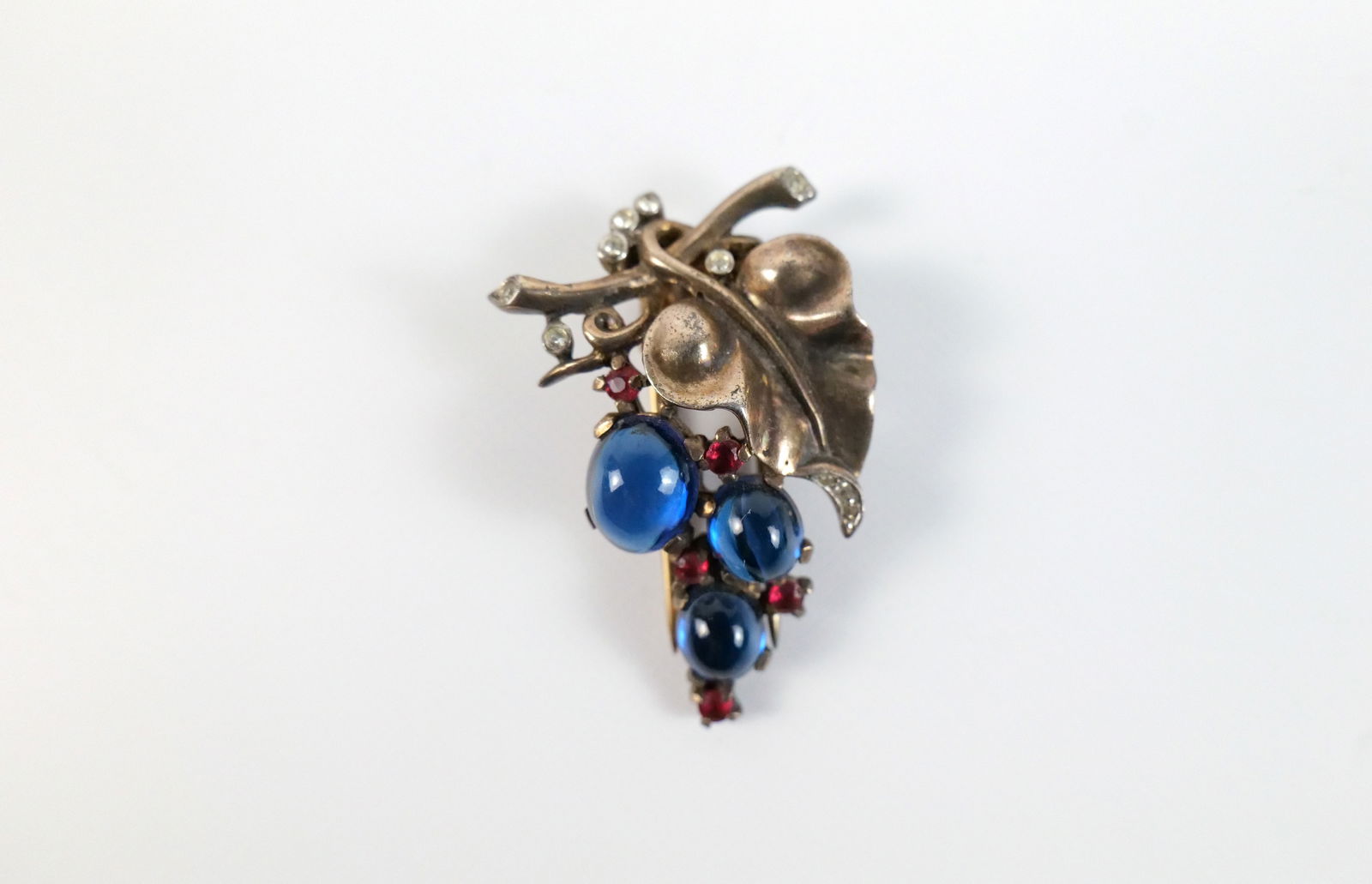 Vintage 1940s Sterling Trifari Grape Fur Clip: Vintage 1940s Sterling Trifari Grape Fur Clip. The lot includes a vintage 1940s 1.77'' x 1.08'' gold vermeil sterling Trifari fur clip in the form of grapes hanging on the vine set with oval blue glas