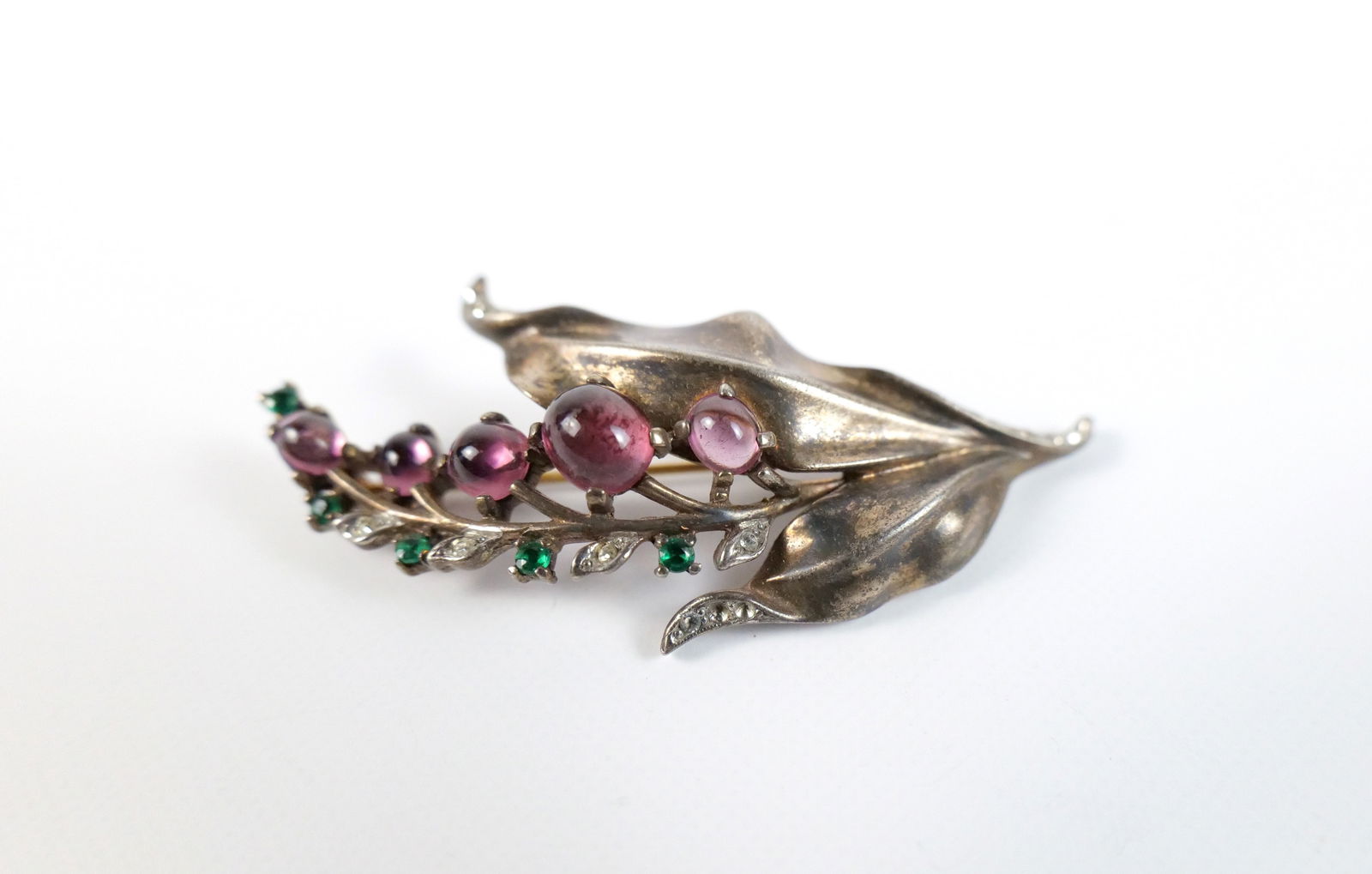 Vintage 1940s Sterling Flower Brooch by Trifari: Vintage 1940s Sterling Flower Brooch byTrifari. The lot includes a vintage 1940s 2.64'' x 1.20'' sterling floral brooch by Trifari set with oal purple glass cabachons and white and green rhinestone ac