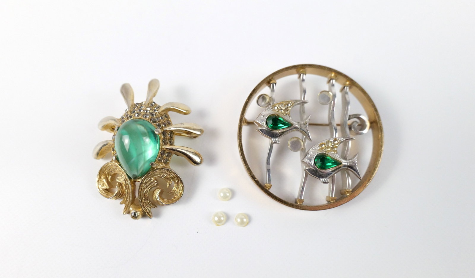 Pair of Midcentury Gold Tone Brooches: Pair of Midcentury Gold Tone Brooches. The lot includes a pair of vintage mid century brooches. Featuring a 1.83'' x 1.42'' crest-like brooch by Les Bernard Inc. with a pear shaped green glass cabocho