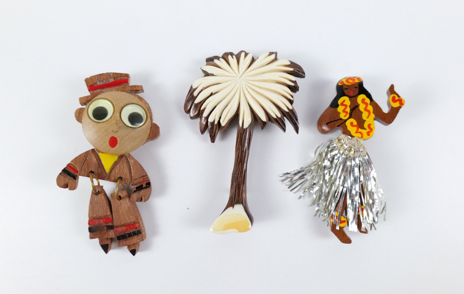 Trio of 1940s Wooden Brooches: Trio of 1940s Wooden Brooches. The lot includes a trio of vintage 1940s wooden brooches. Featuring a 3'' x 1.45'' wooden hula dancer brooch with hand painted details, a metal tinsel skirt, and a hinge