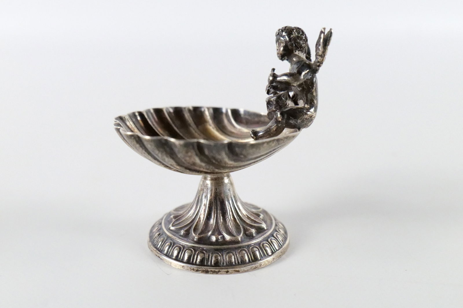 Antique Silver Scalloped Shape Salt Cellar with Cupid: Antique Silver Scalloped Shape Salt Cellar with Cupid. At least 800 silver. No Markings. Measures 2" tall x 2" wide. All invoices must be paid within 24 hours of the sale. We offer multiple shipping o