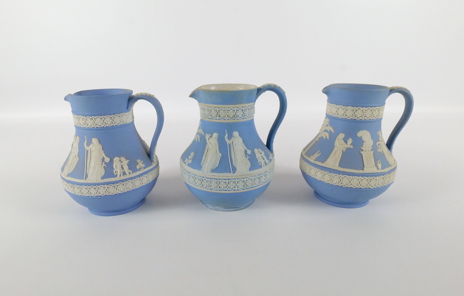 Lot of 3 Wedgwood Blue Jasperware Pitchers: Lot of 3 Wedgwood Blue Jasperware Pitchers. One is Antique Dipped and the Others are Solid. All depicting Neoclassical Scenes. Measures 5.25". All invoices must be paid within 24 hours of the sale. We