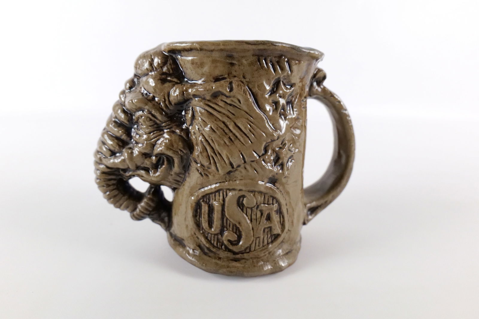 Jim Rumph Art Pottery Political Mug: Jim Rumph Art Pottery Political Mug. Depicting a Republican Elephant with Tied Up Donkey inside and USA on the other side of the mug. Dated 1971. Measures 5.25" tall. All invoices must be paid within