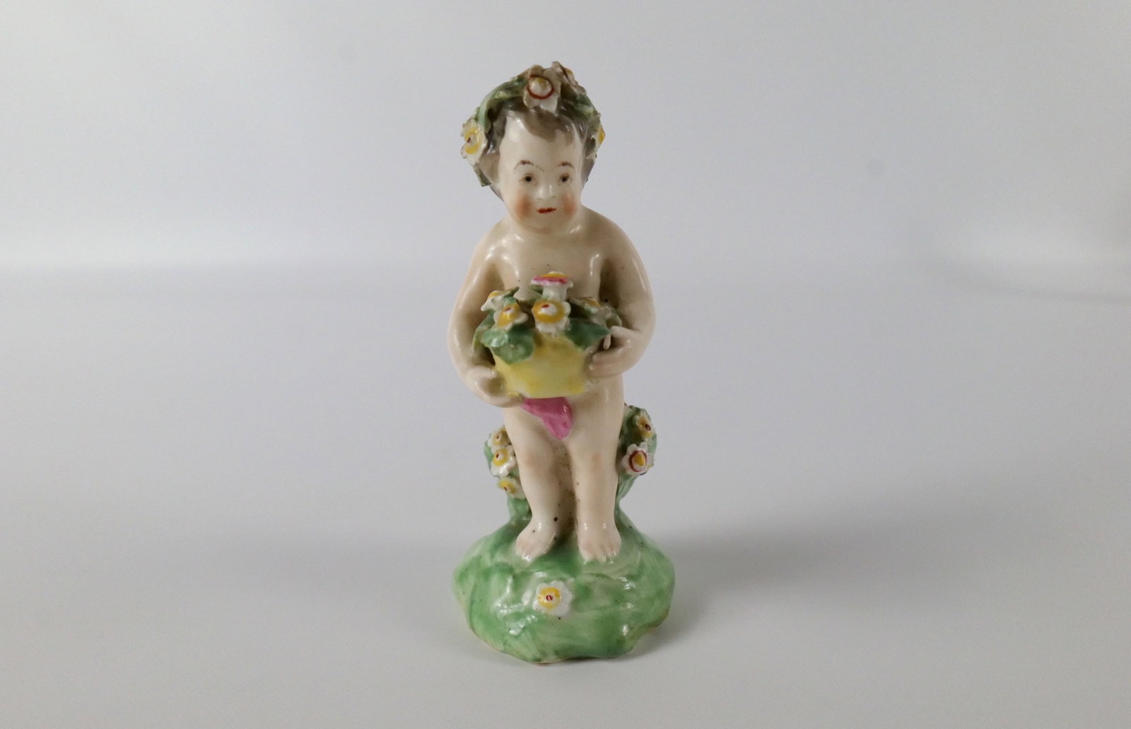 18th Century Porcelain Putti Figurine: 18th Century Porcelain Putti Figurine. Unsigned - Possibly Derby. Chips to flowers and leaves and some loss to glaze. Head has been totally repaired. Measures 4" tall. All invoices must be paid within