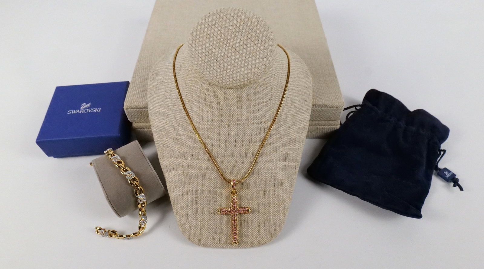 Gold Tone Swarovski Cross Pendant Necklace and More: Gold Tone Swarovski Cross Pendant Necklace and More. The lot includes an adjustable 17'' long gold tone snake chain with a gold tone cross pendant studded with light pink crystal rhinestones by Swarov