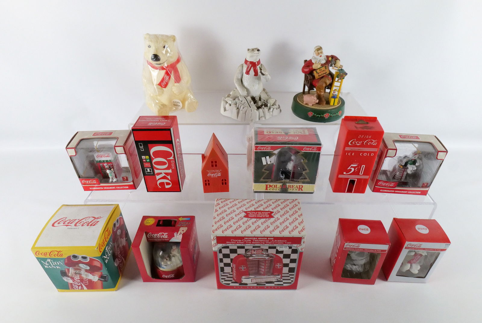 Group Lot of Coca-Cola Decorative Items: Group Lot of Coca-Cola Decorative Items. Including Polar Bear Coin Bank - Factory Sealed, Tabletop Jukebox in Box, Vintage Plastic Banks, and Christmas Ornaments - New in Box. Largest measures 9" tall
