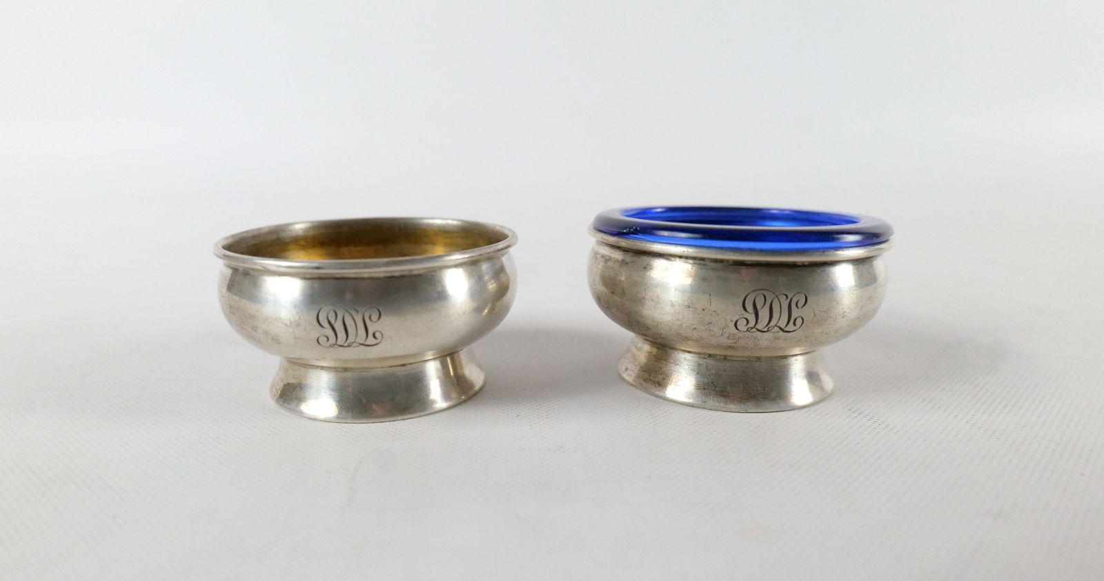 Pair of Tiffany & Co. Sterling Silver Table Salts: Pair of Tiffany & Co. Sterling Silver Table Salts. One Monogramed. One has cobalt insert. Insert has some chipping on rim. Weighs approx. 71.6 grams without insert. Measures 1" tall x 2.25" wide. All